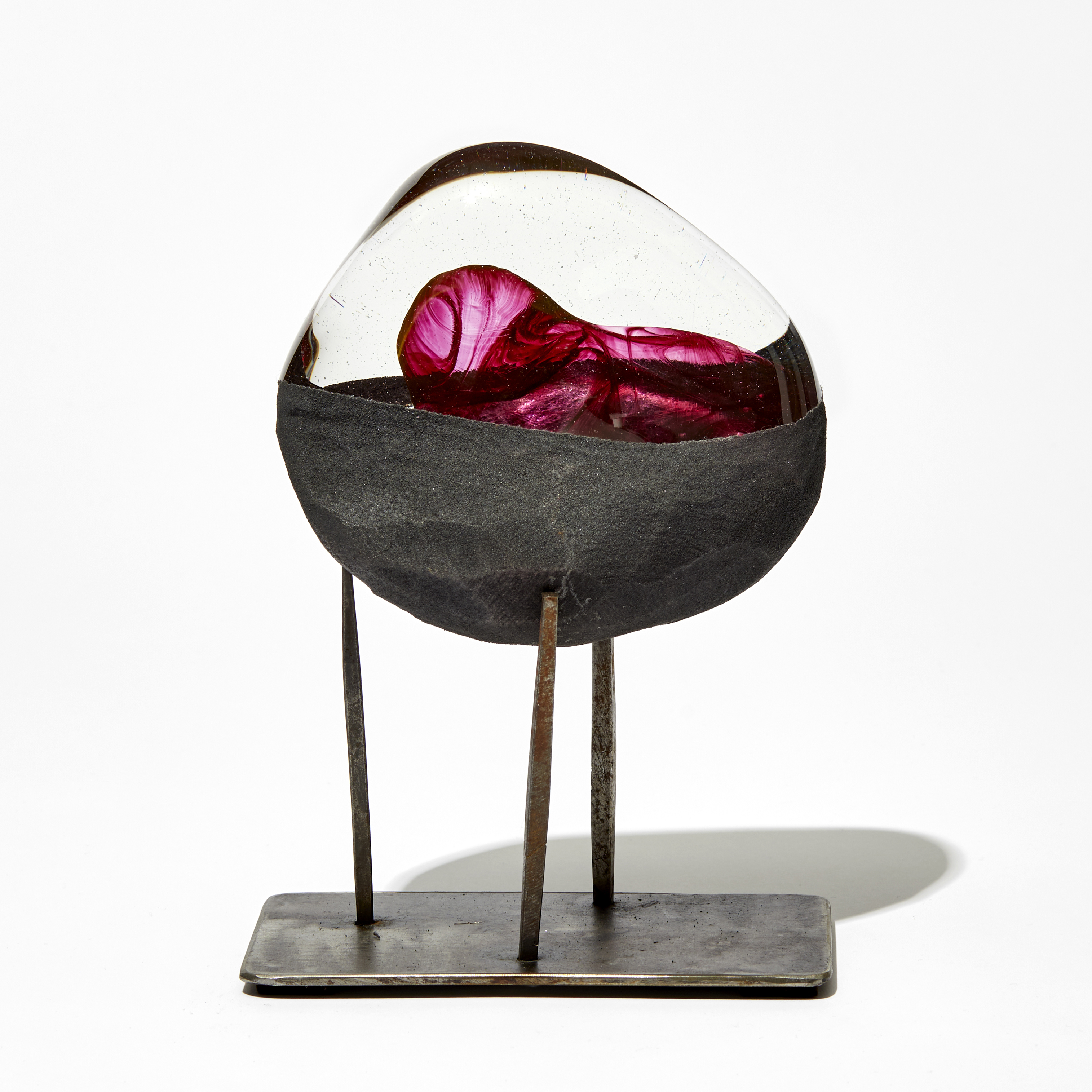 clear and matt metallic grey rounded mass with swirling red core placed on a three pronged steel base