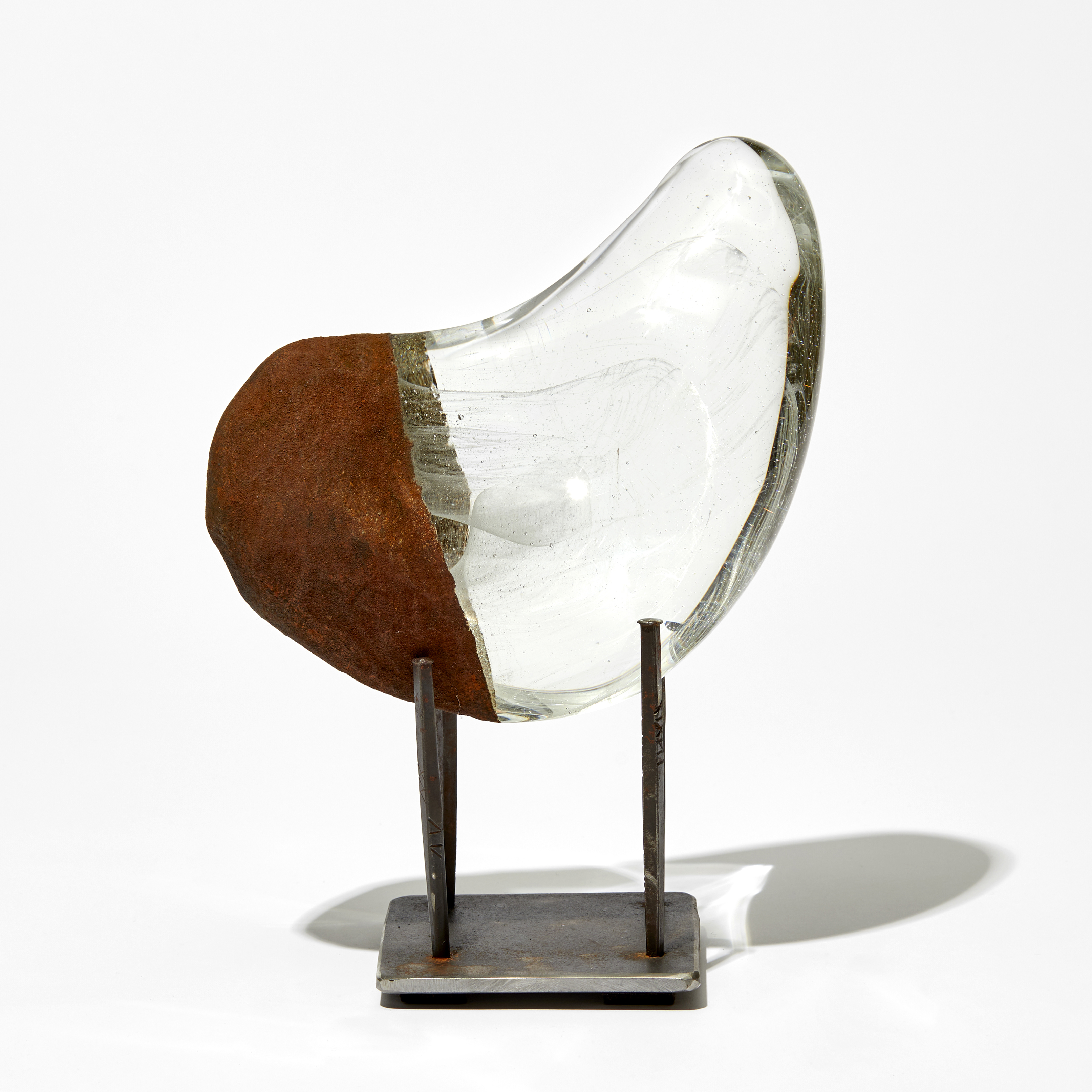 clear and opaque rust curved sculpture with fine wispy inner detail handmade from glass on a three pronged steel base
