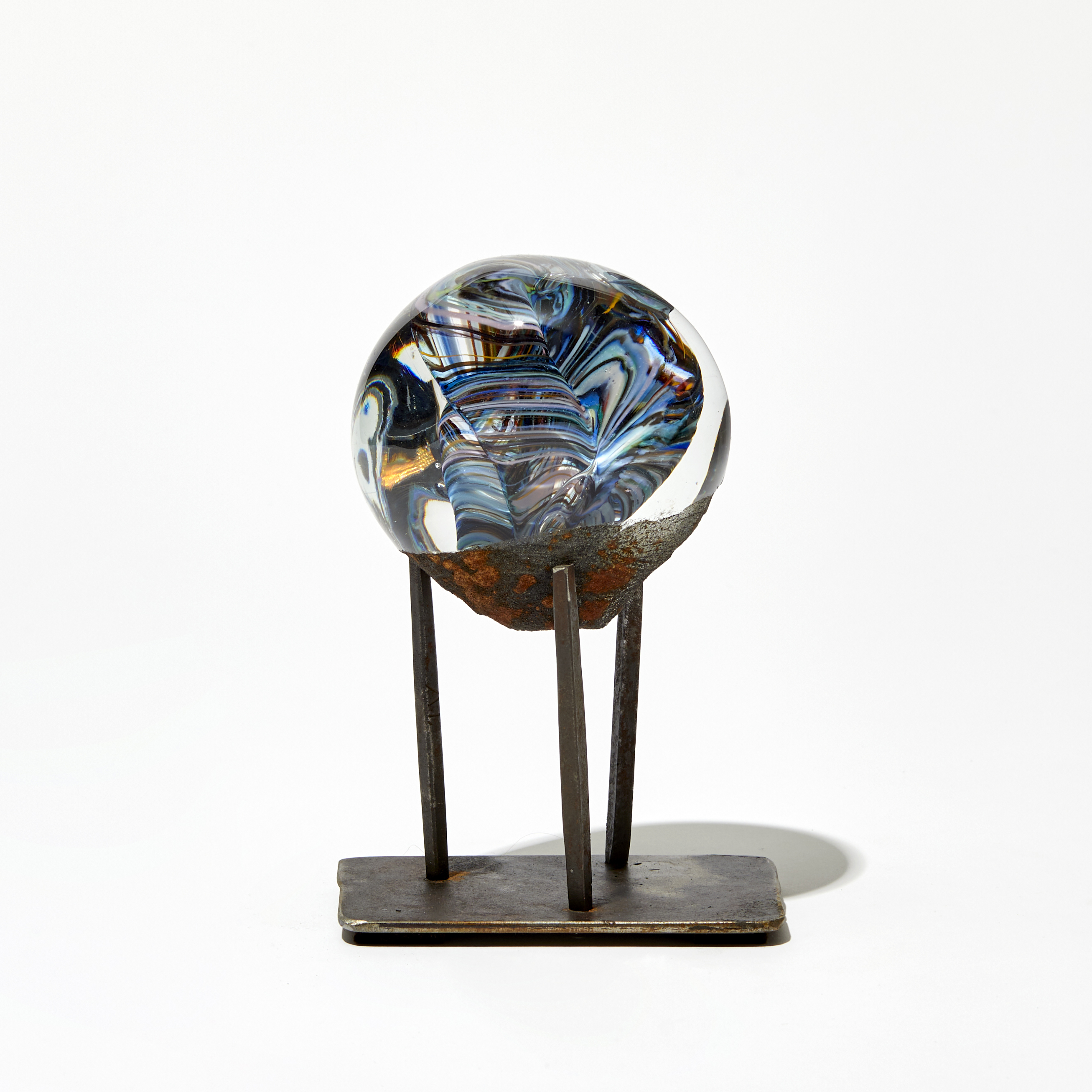 marble like round glass sculpture in clear blue and rust brown on three pronged steel base