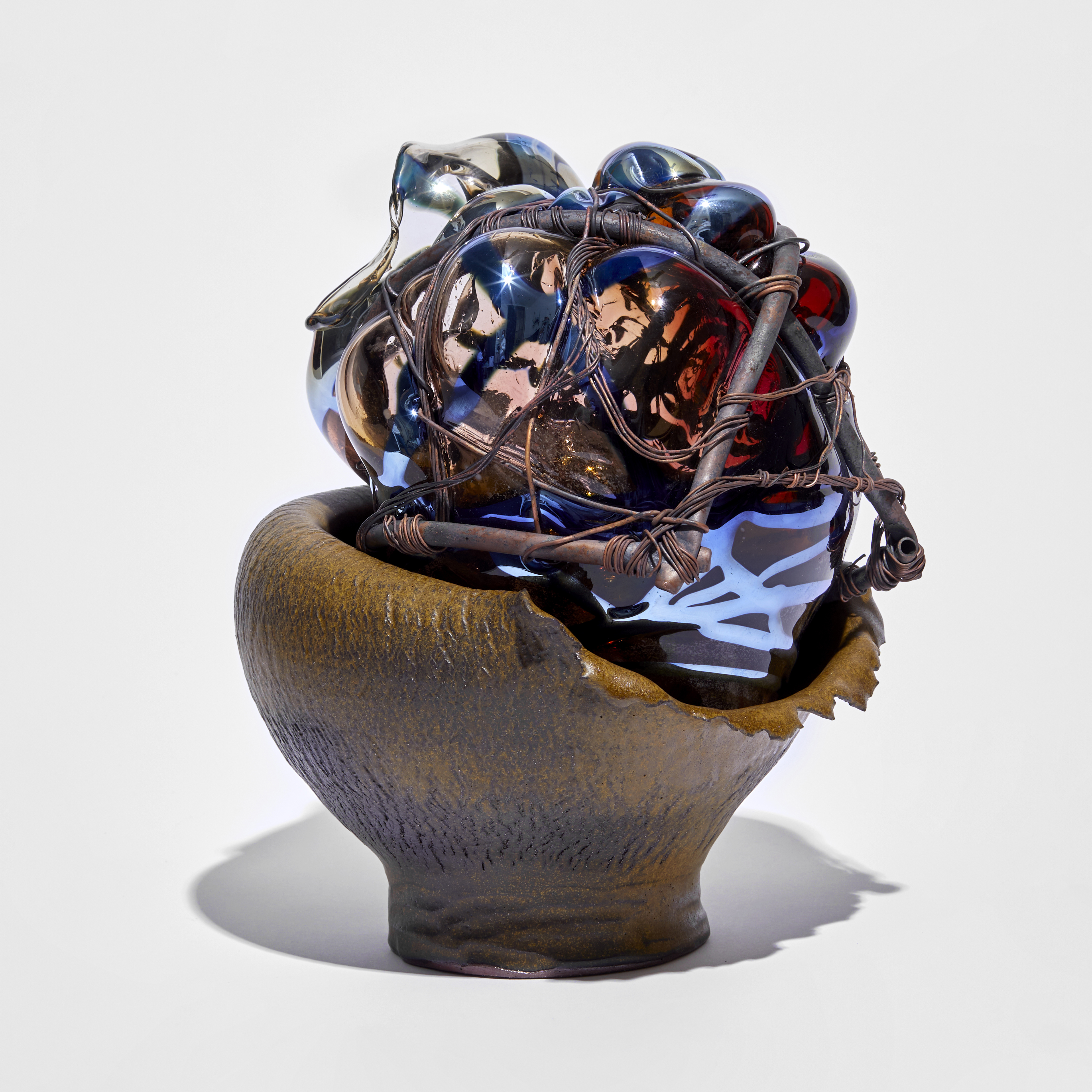 rich down wrinkled bowl with leathery appearance cradling a mass of pink and blue glass bound in copper