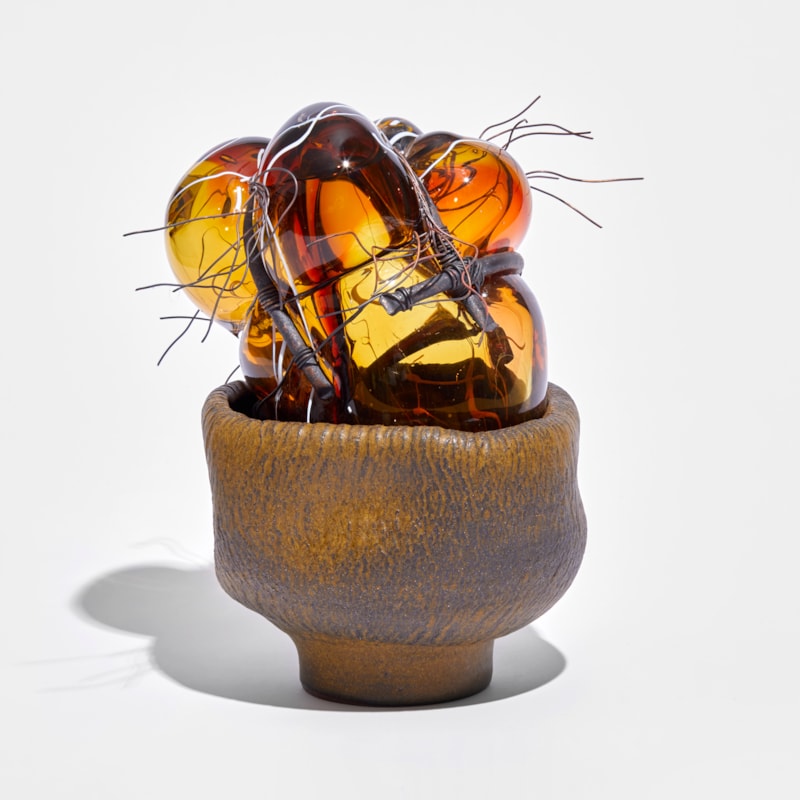 terracotta leathery looking low bowl filled with bubbled amber glass bound in copper pipe and wire