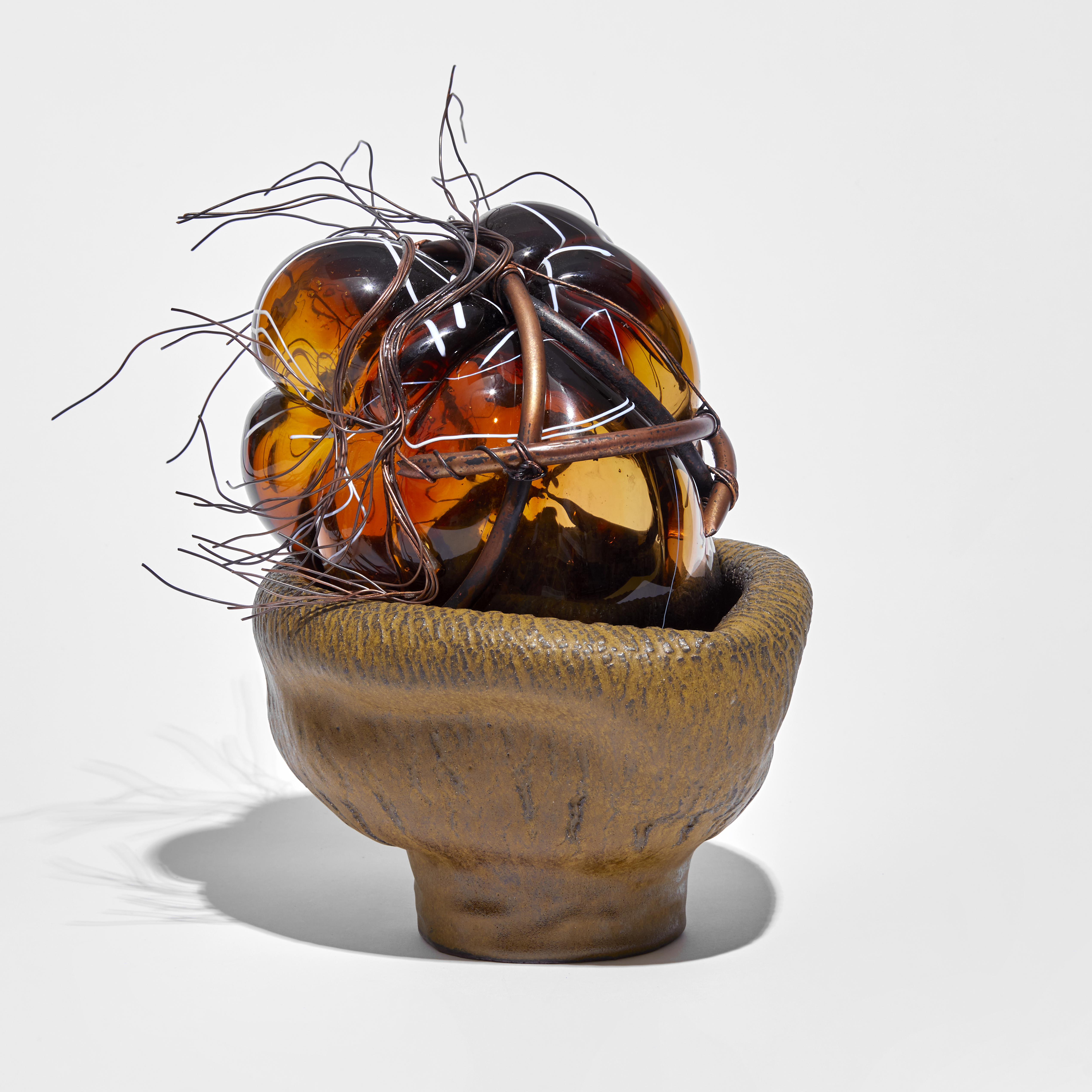 leathery looking ceramic base holding an amorphous mass of rich amber glass bound in copper pipe and wire handmade
