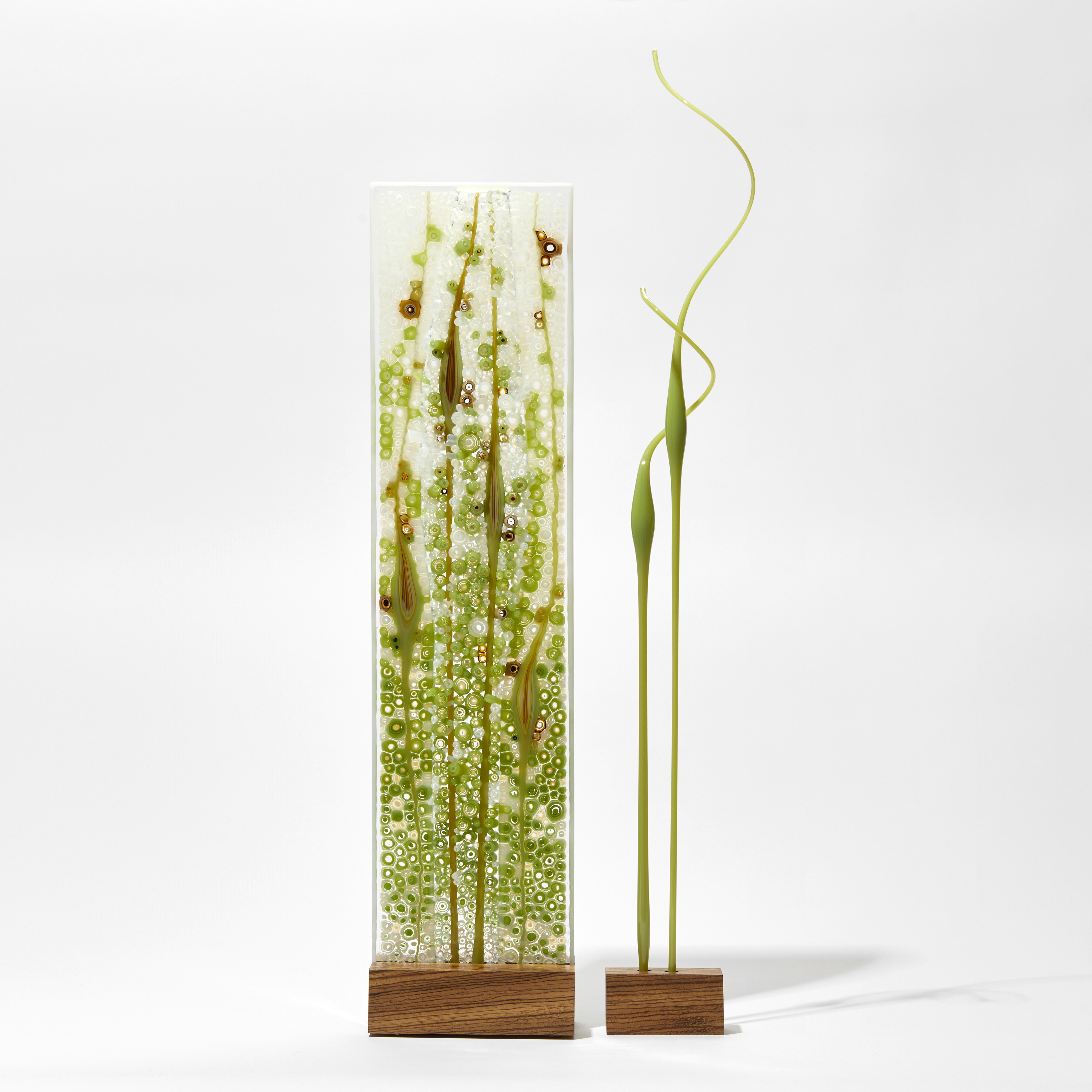 green turquoise and white flat glass panel on wooden stand with separate curling coloured rods of glass on their own stand