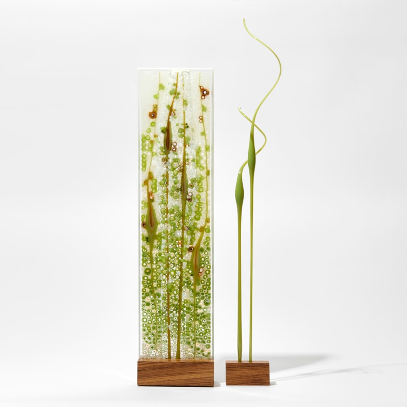 green turquoise and white flat glass panel on wooden stand with separate curling coloured rods of glass on their own stand