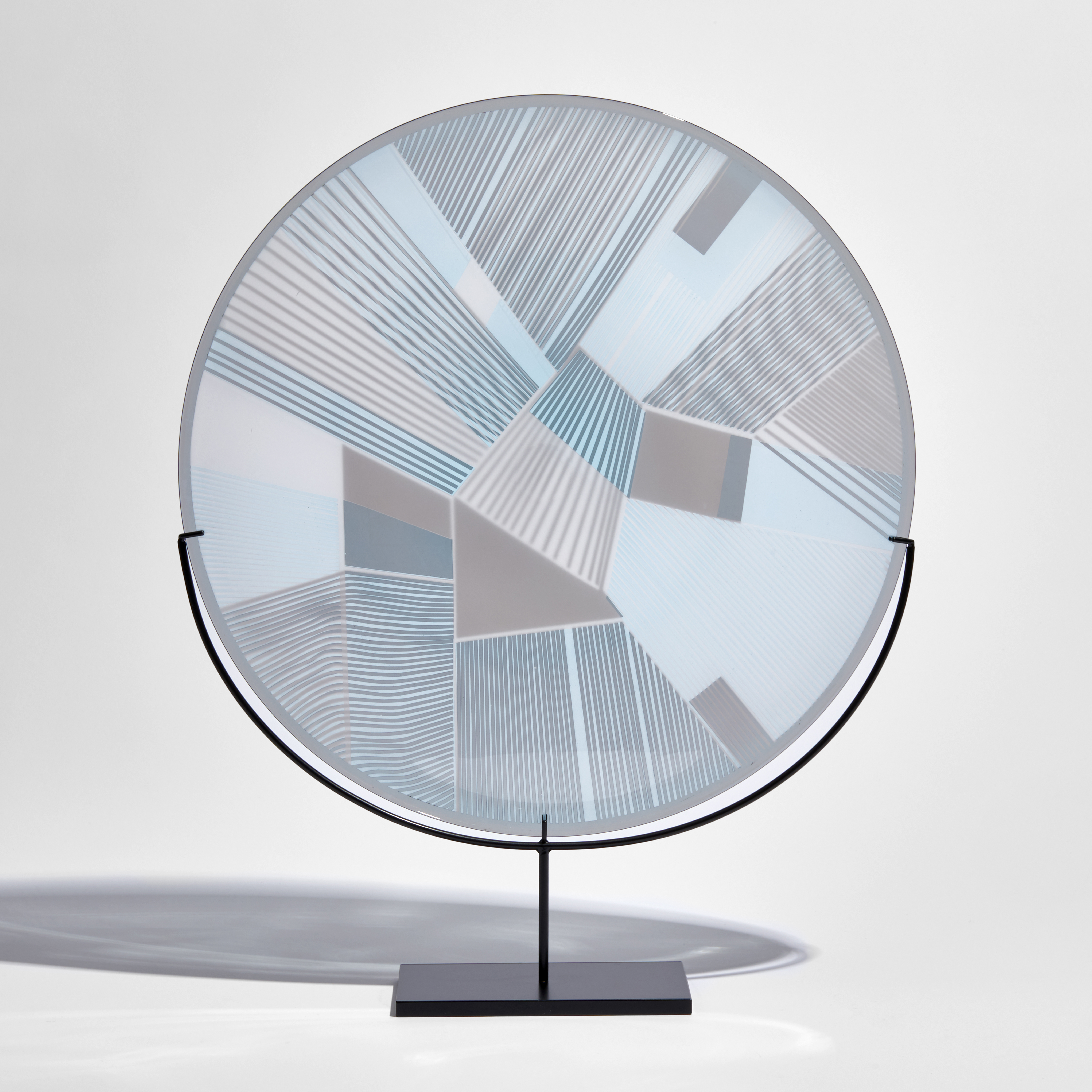 round glass plate with etched graphic pattern on the surface in soft blue and grey on a black metal stand