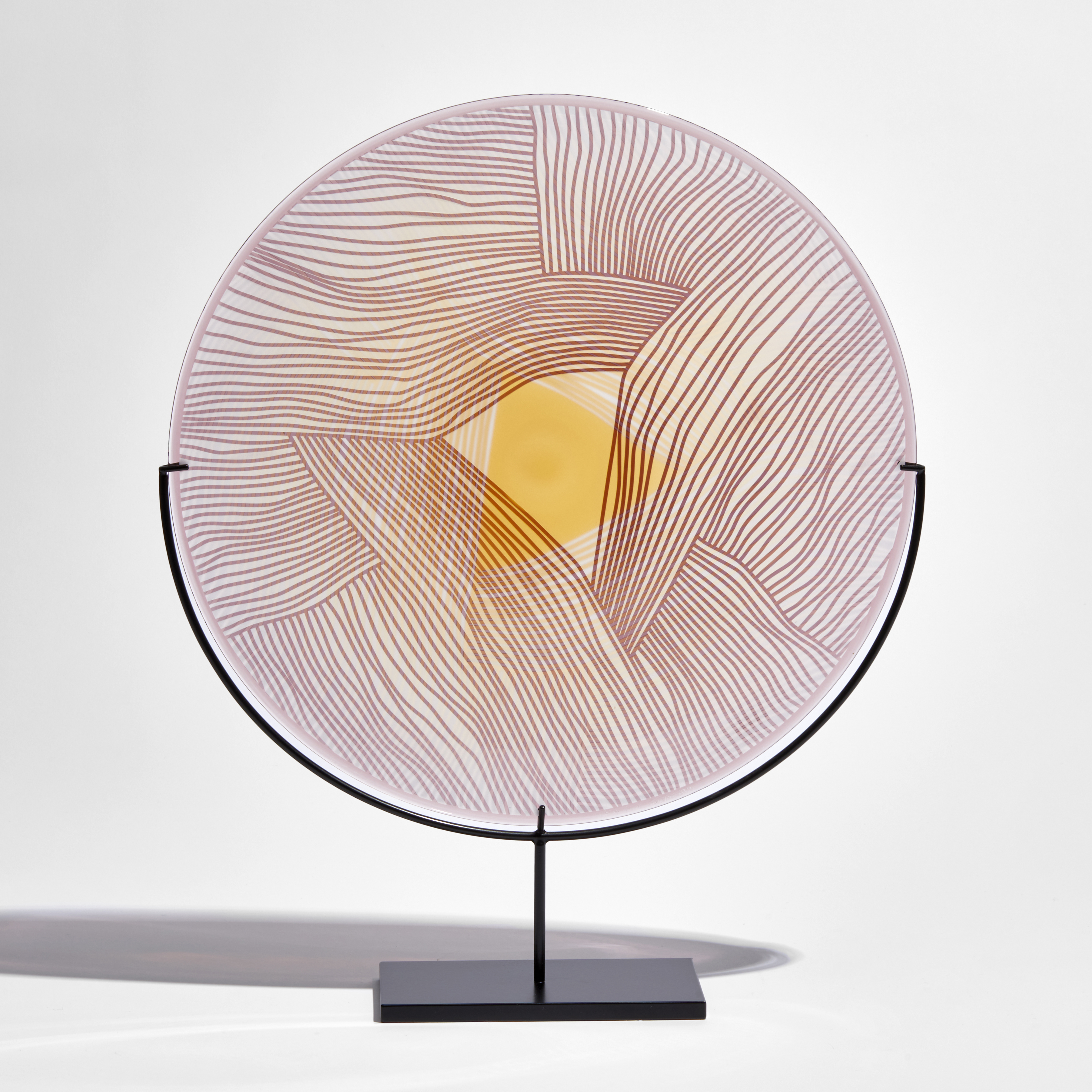 round plate in gold red and clear glass with cut raised meandering lines on a black metal stand