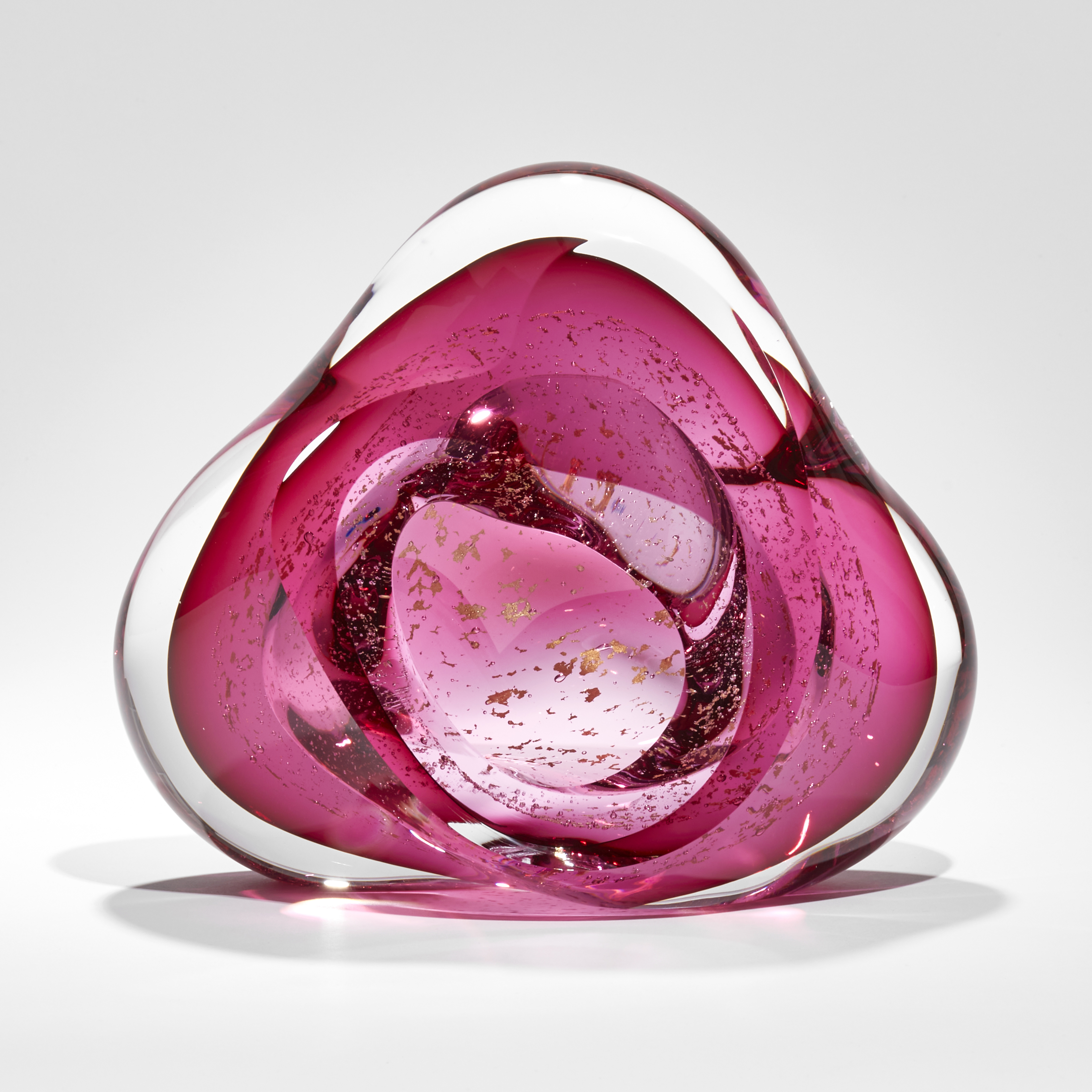 soft triangular glass sculpture with clear outer and bright pink inner layer containing trapped small fragments of 24 carat gold