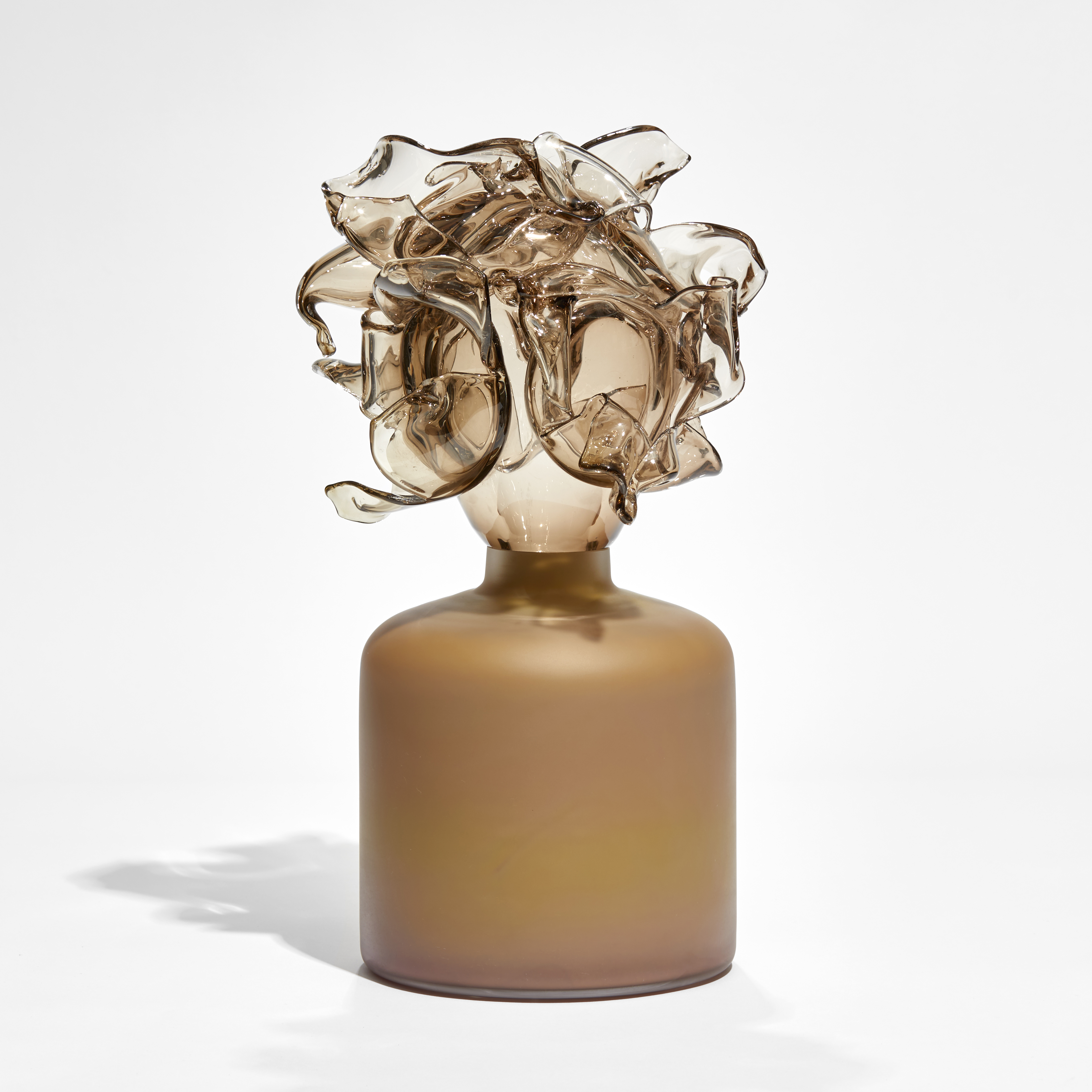 low caramel coloured round cylindrical base with abstract floral explosion perched on the top in bronze tint hand made from glass