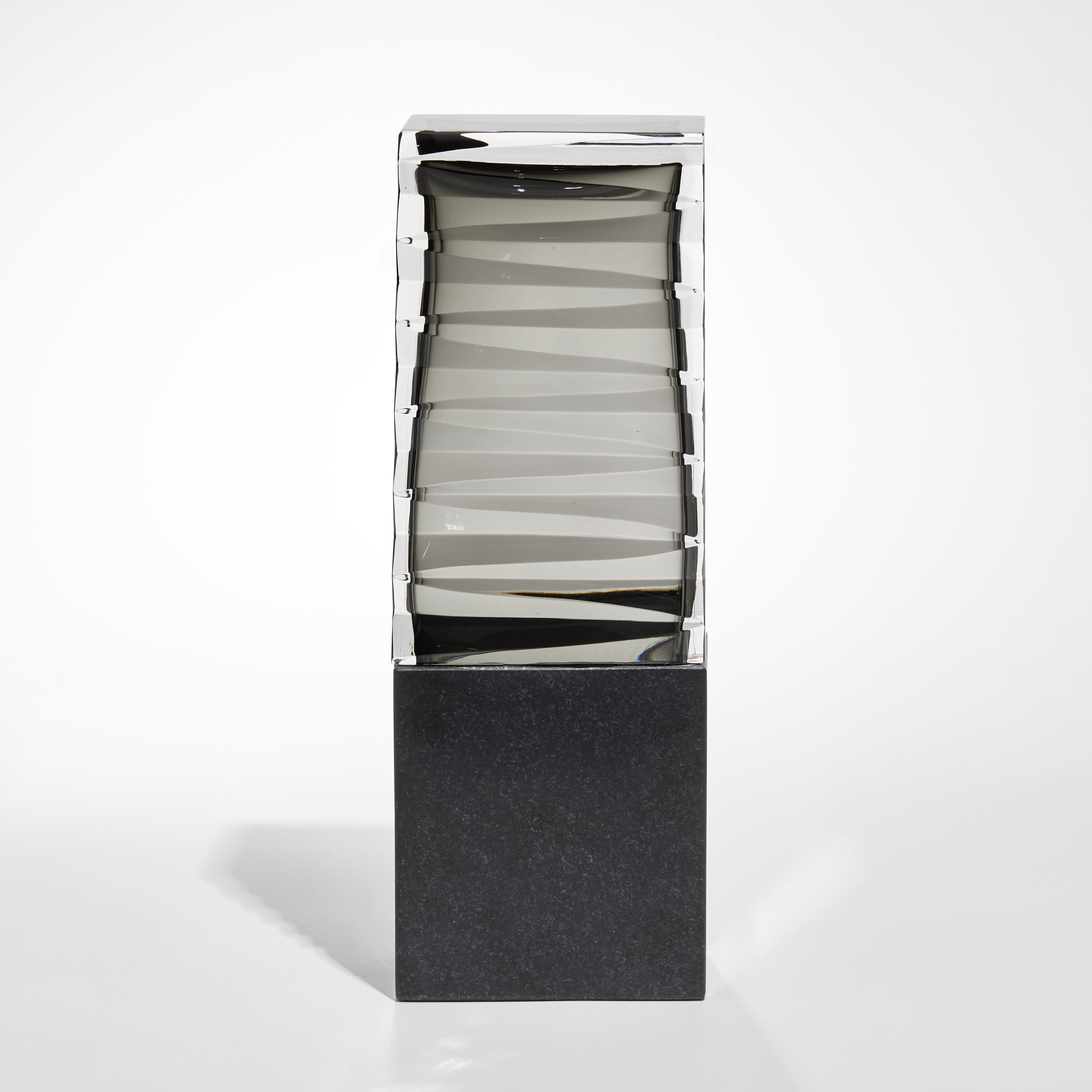 standing rectangular sculpture with black stone base and smokey grey top with inner folded origami detail hand made from glass