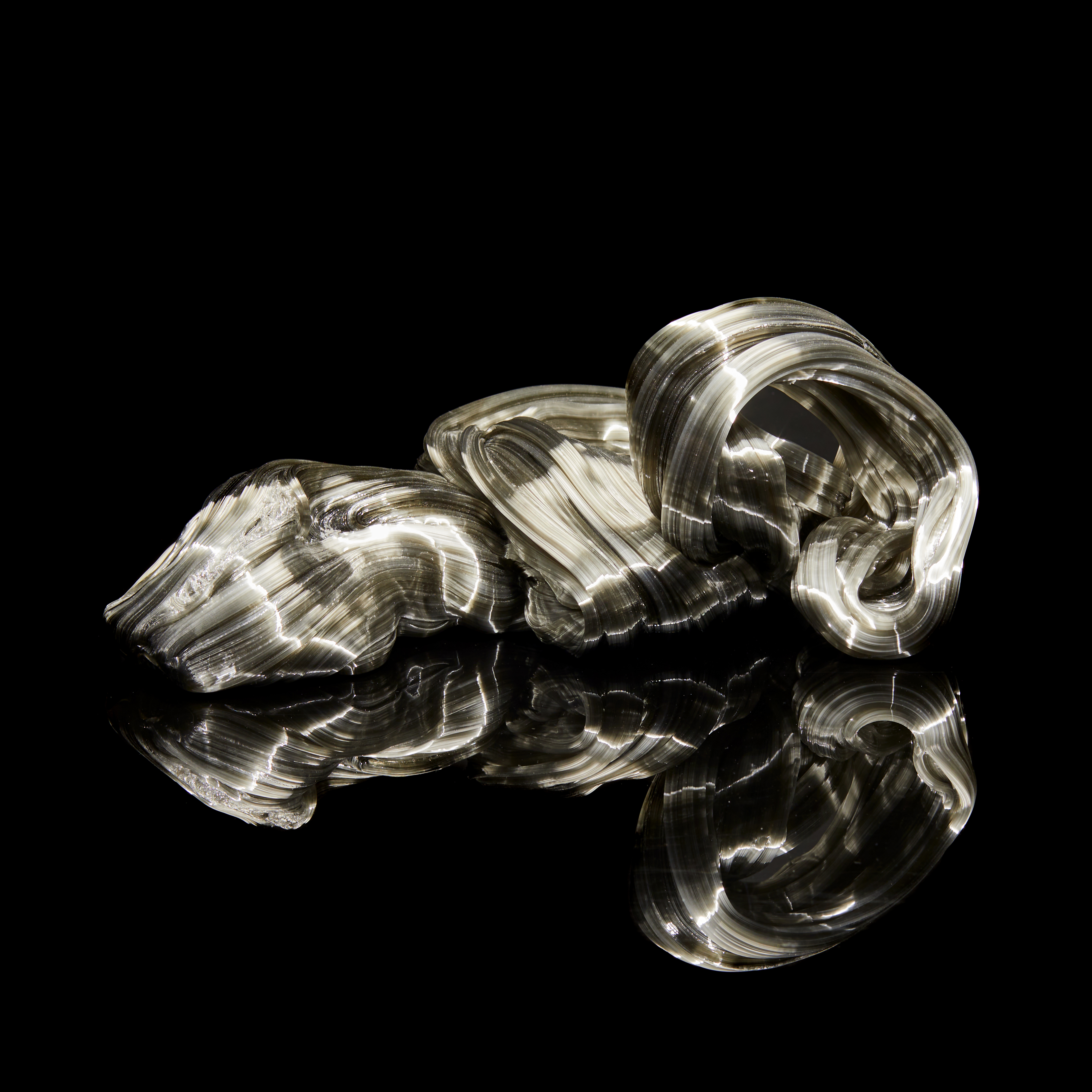 ooozing mass of smokey grey glass with ridged surface twisting and flat along the floor