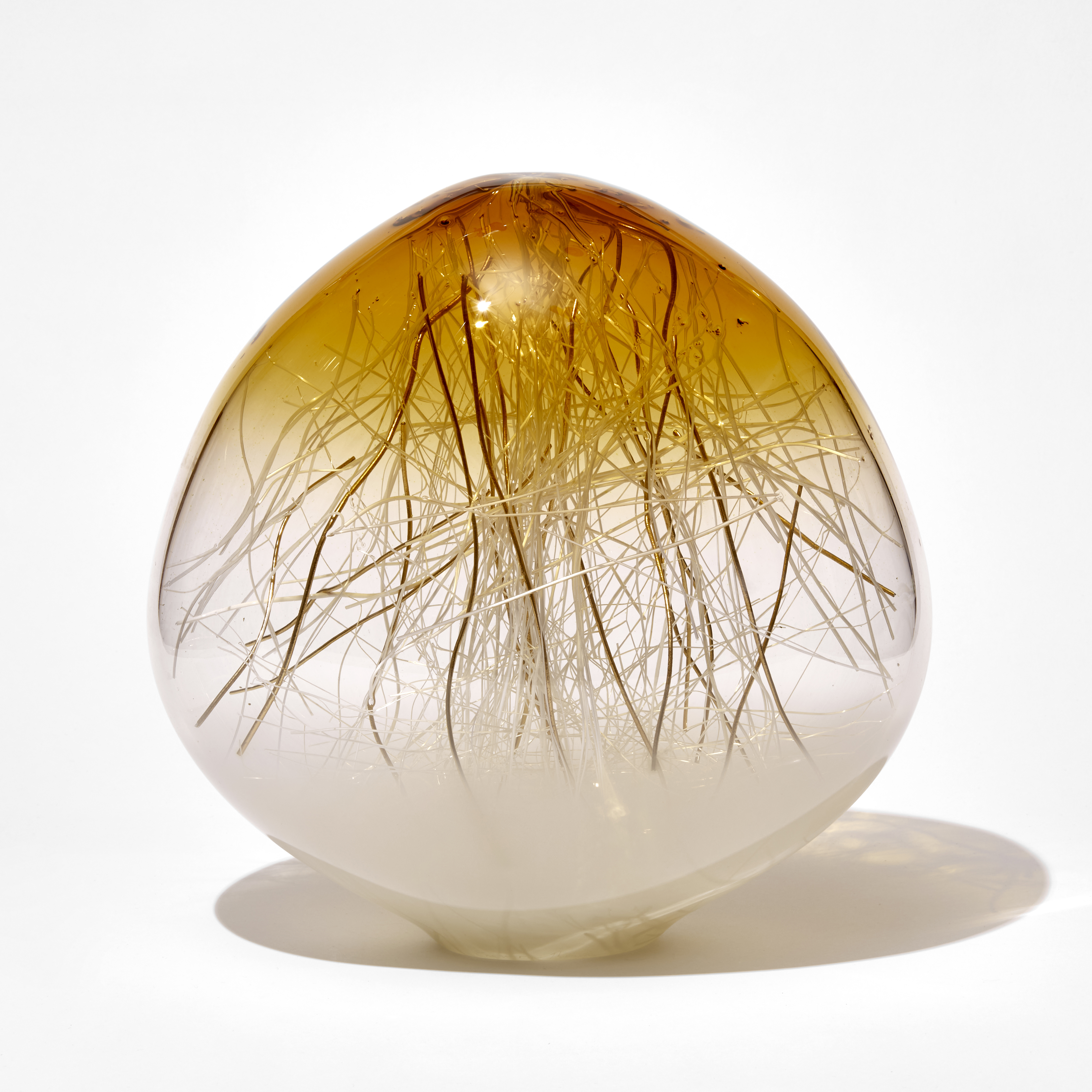 rounded sculpture with slightly pointed top fading from white clear and amber top containing thin canes in white and gold hand made from glass 