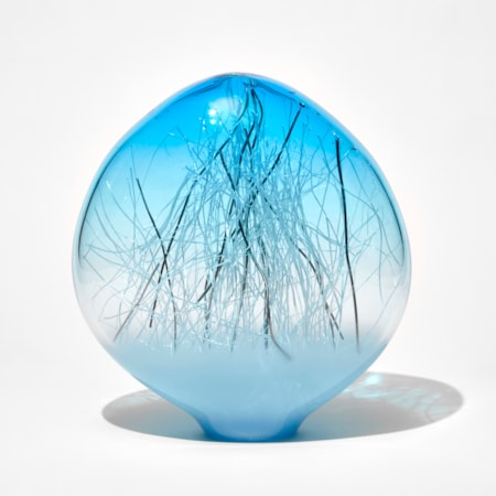 low ovoid hand made glass sculpture with soft blue base fading to clear to a bright aqua top with thin canes in white and platinum trapped inside
