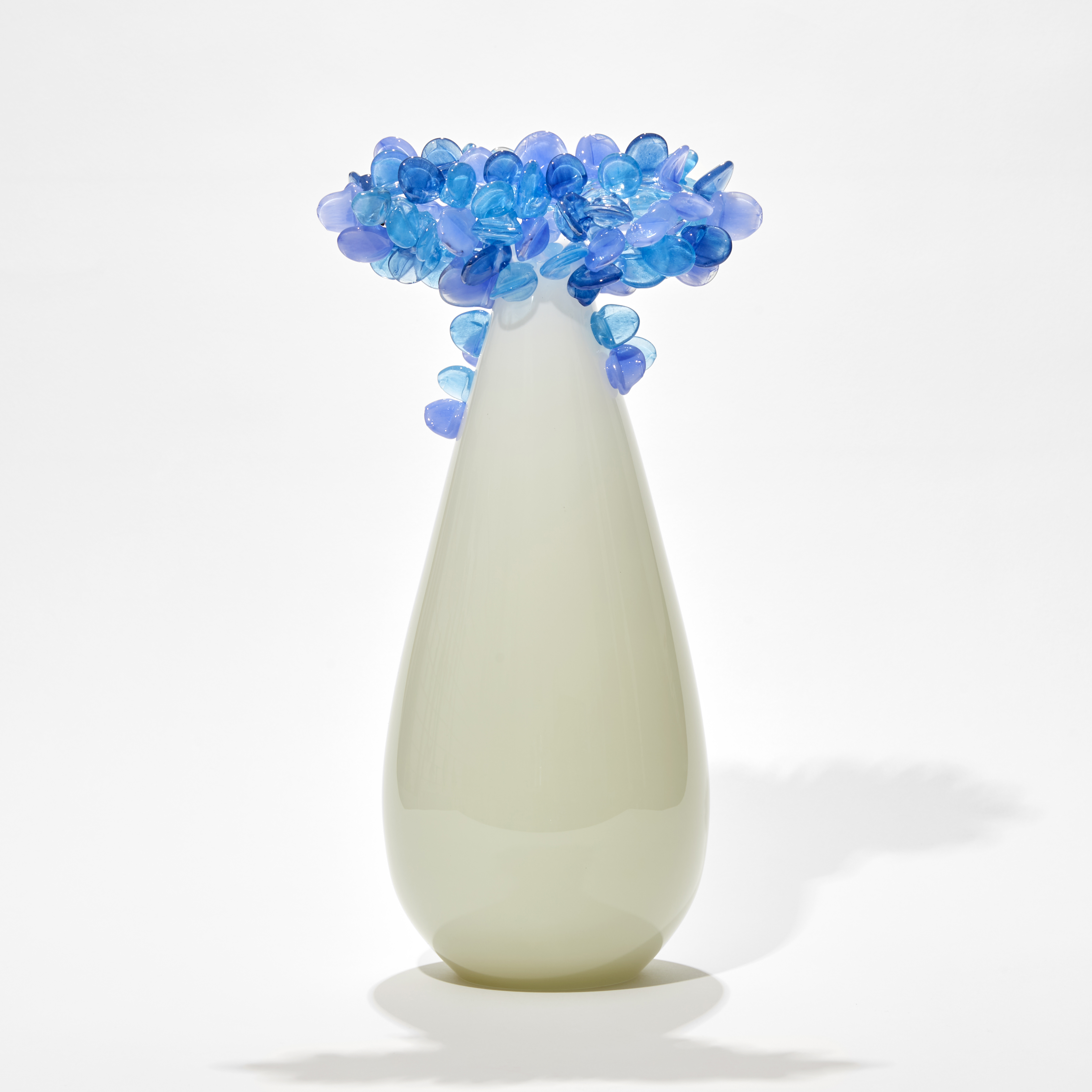 tree with teardrop shaped trunk in off white alabaster with a cluster of perched rounded leaves in soft blues and light lilac hand made from glass
