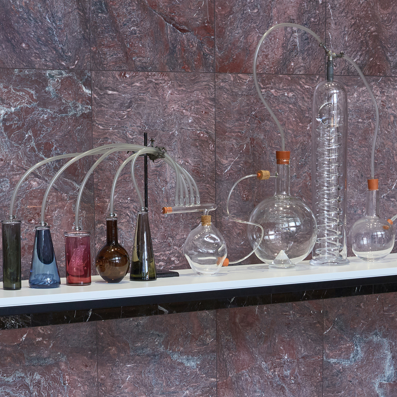sculptural installation with scientific bottles connected by tubes with rubber bungs hand made from glass some with colour some in just clear