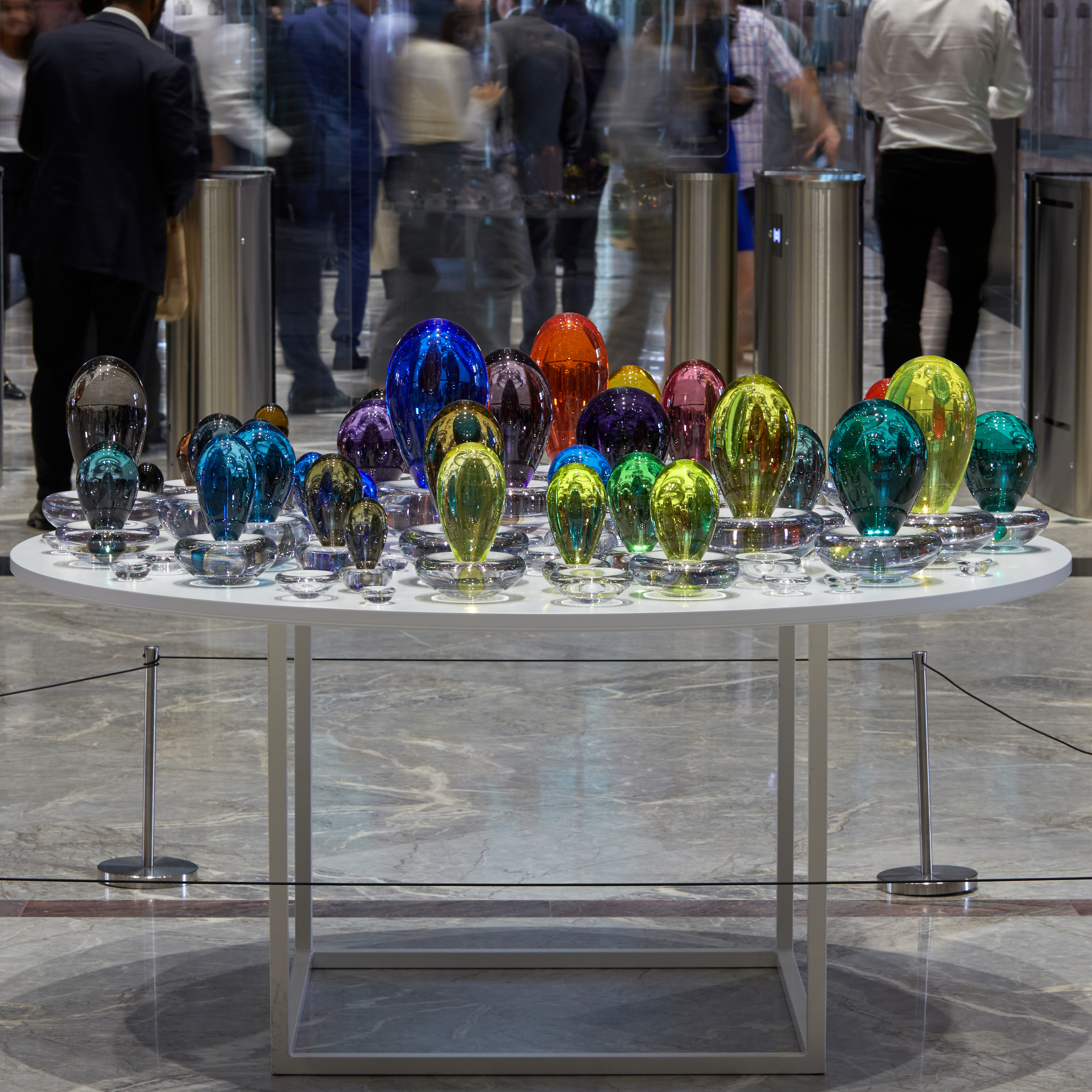 an installation consisting of a multitude of coloured droplets with a clear base each one a different colour creating a rainbow of hues handmade from glass