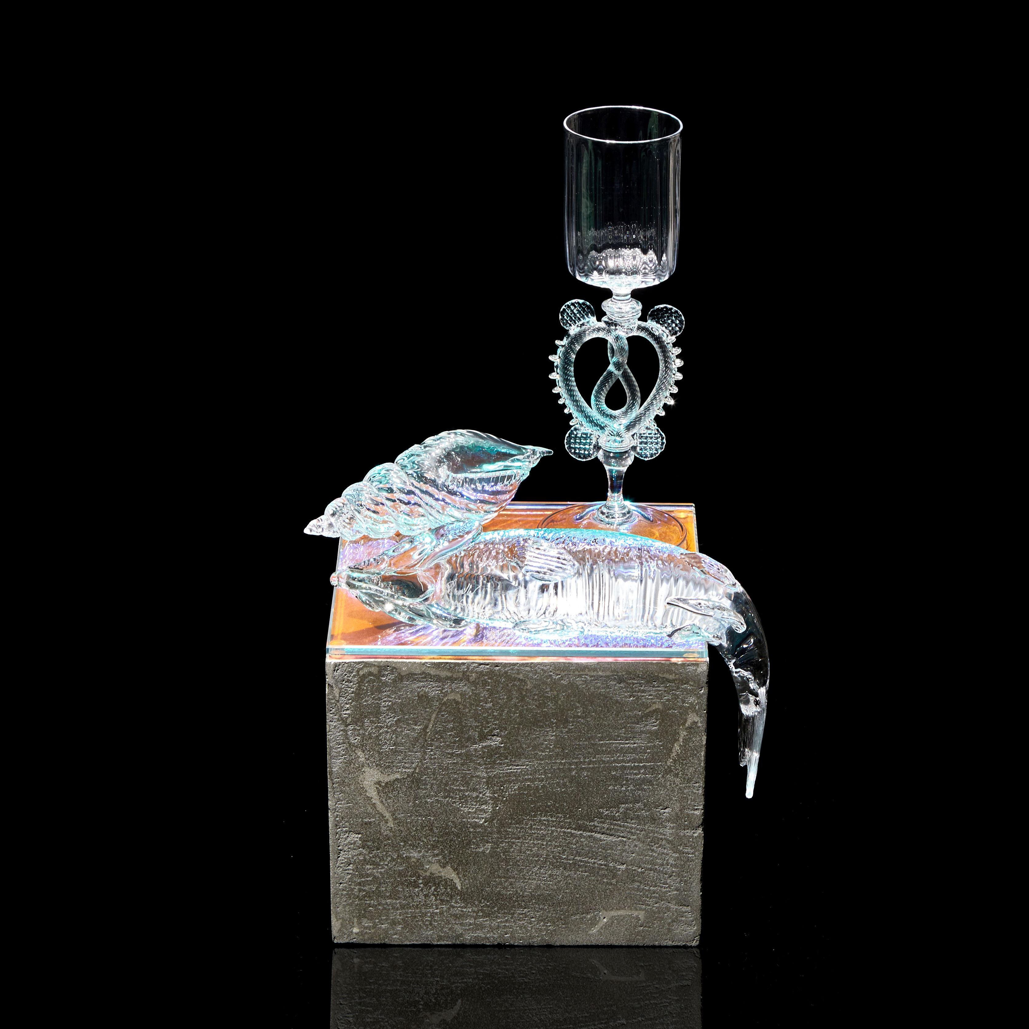 three dimensional still life with goblet shell and fish sitting on a grey concrete effect plinth handmade from glass