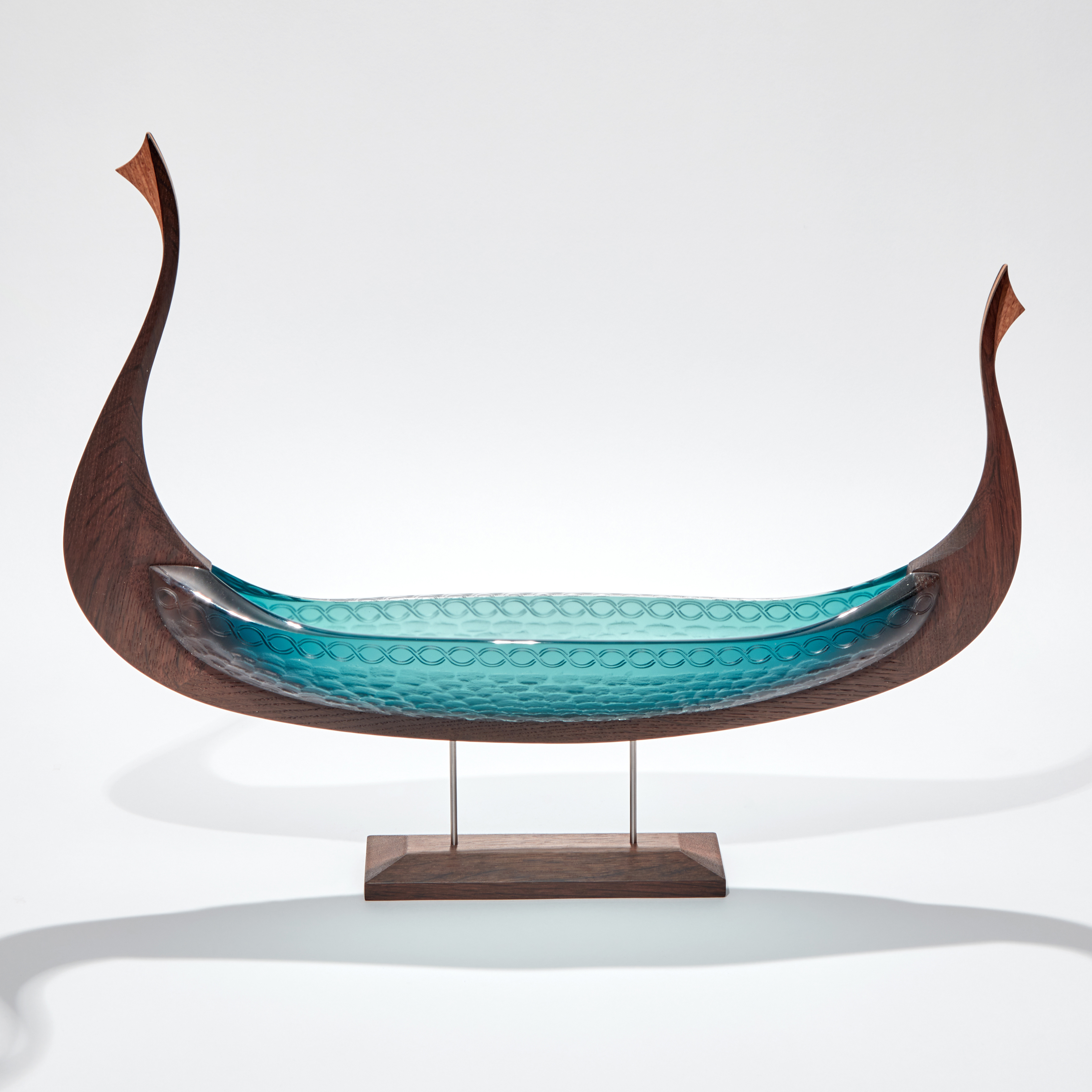 viking ship made from hand carved oak and handblown teal coloured glass with circular cutting detail raised up in a stand