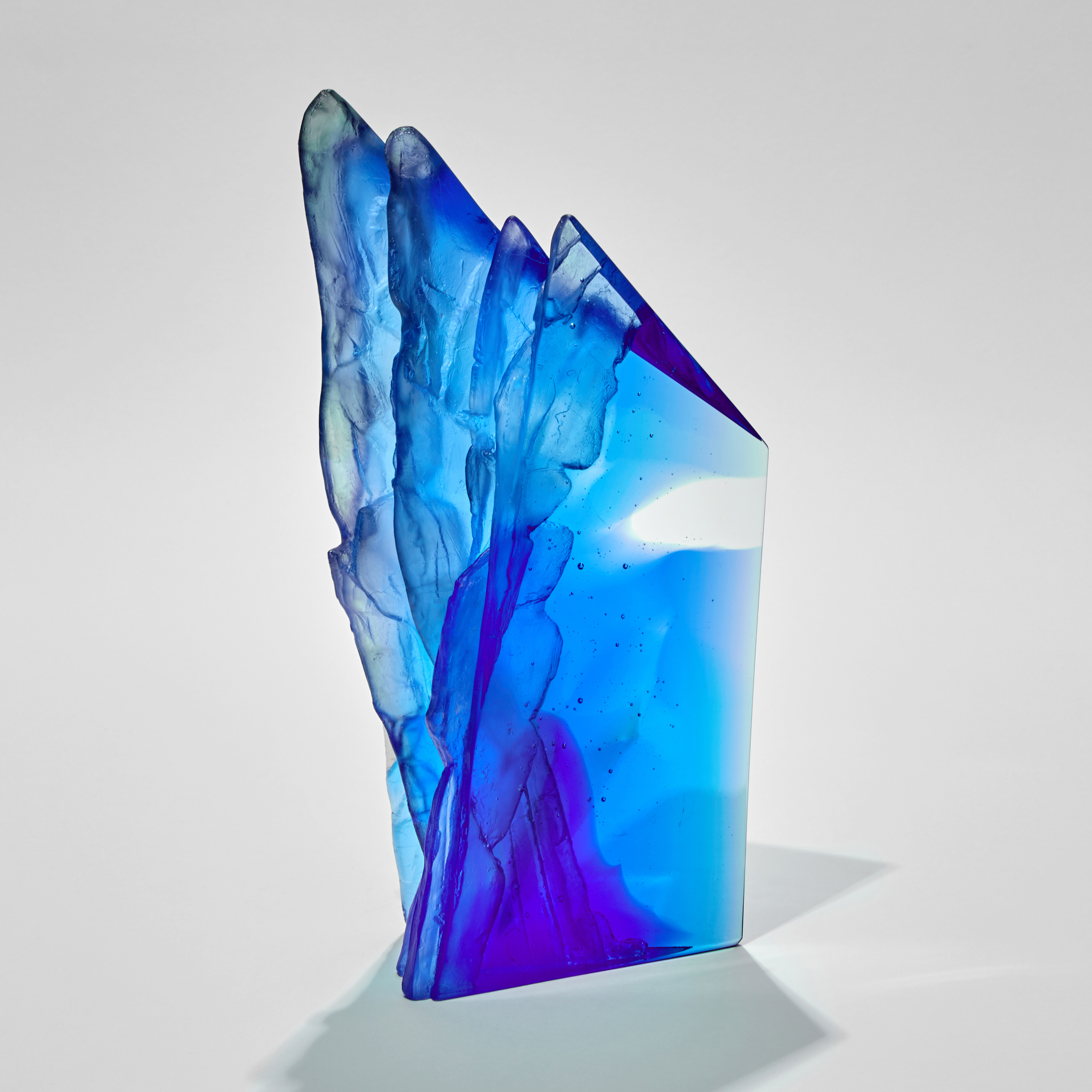 asymmetric mixed blues standing sculpture emulating a cliff face with two sides smooth and one ridged and textured hand made from glass