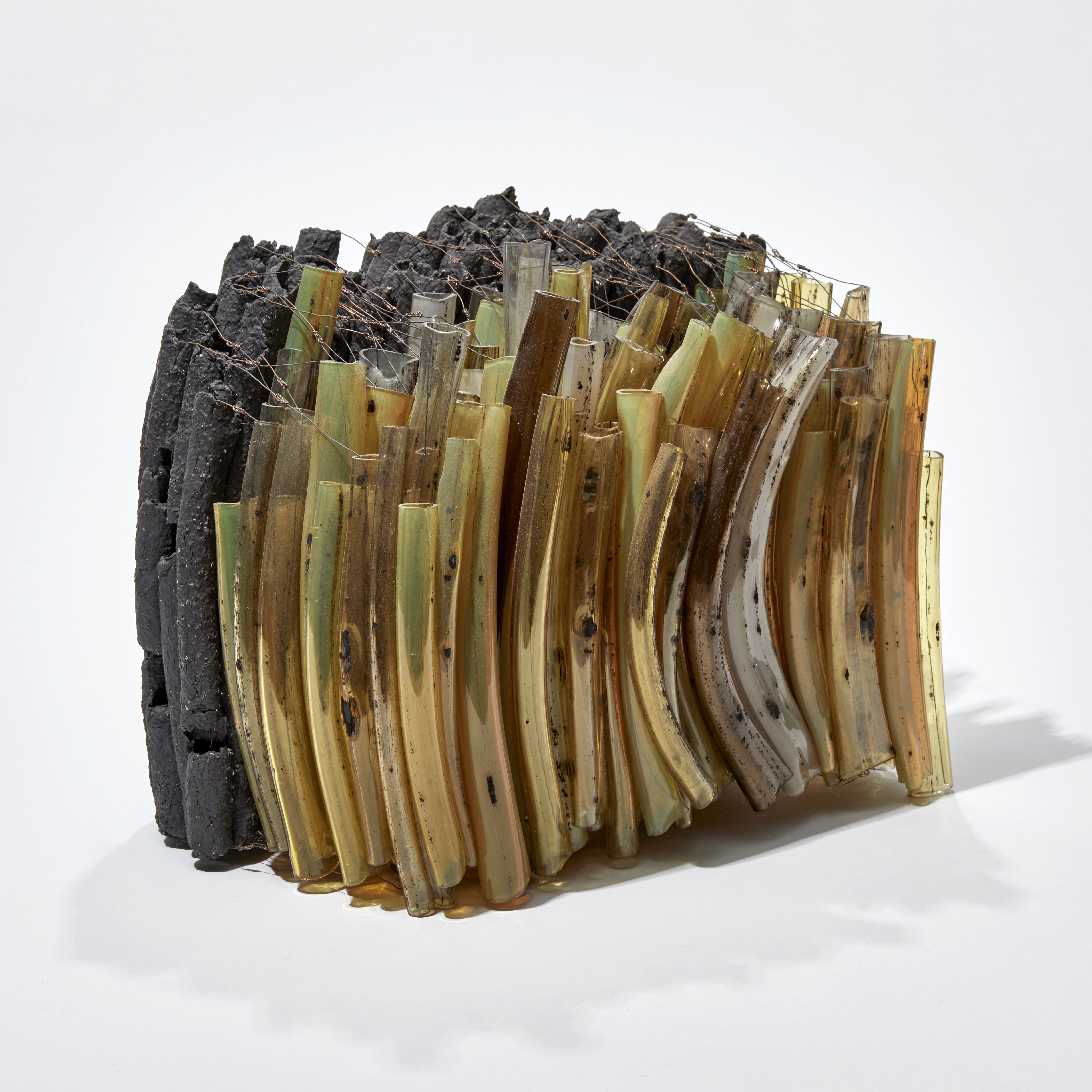 abstract glass art sculpture of long thin lines bunched together in a loose rectangular shape in dark green orange and black