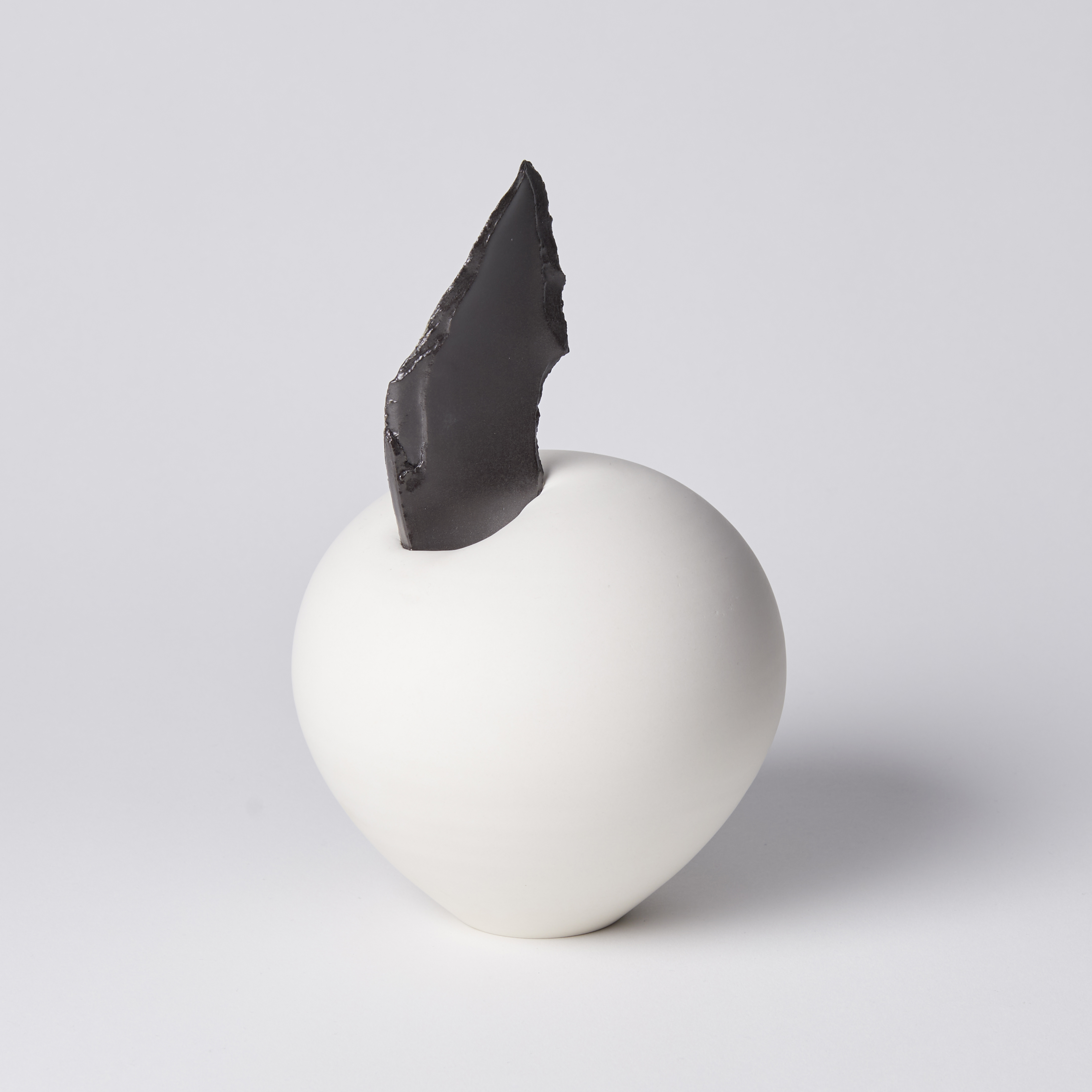 white rounded shape with black rough edge shard jammed in the top piecing the form hand made from porcelain