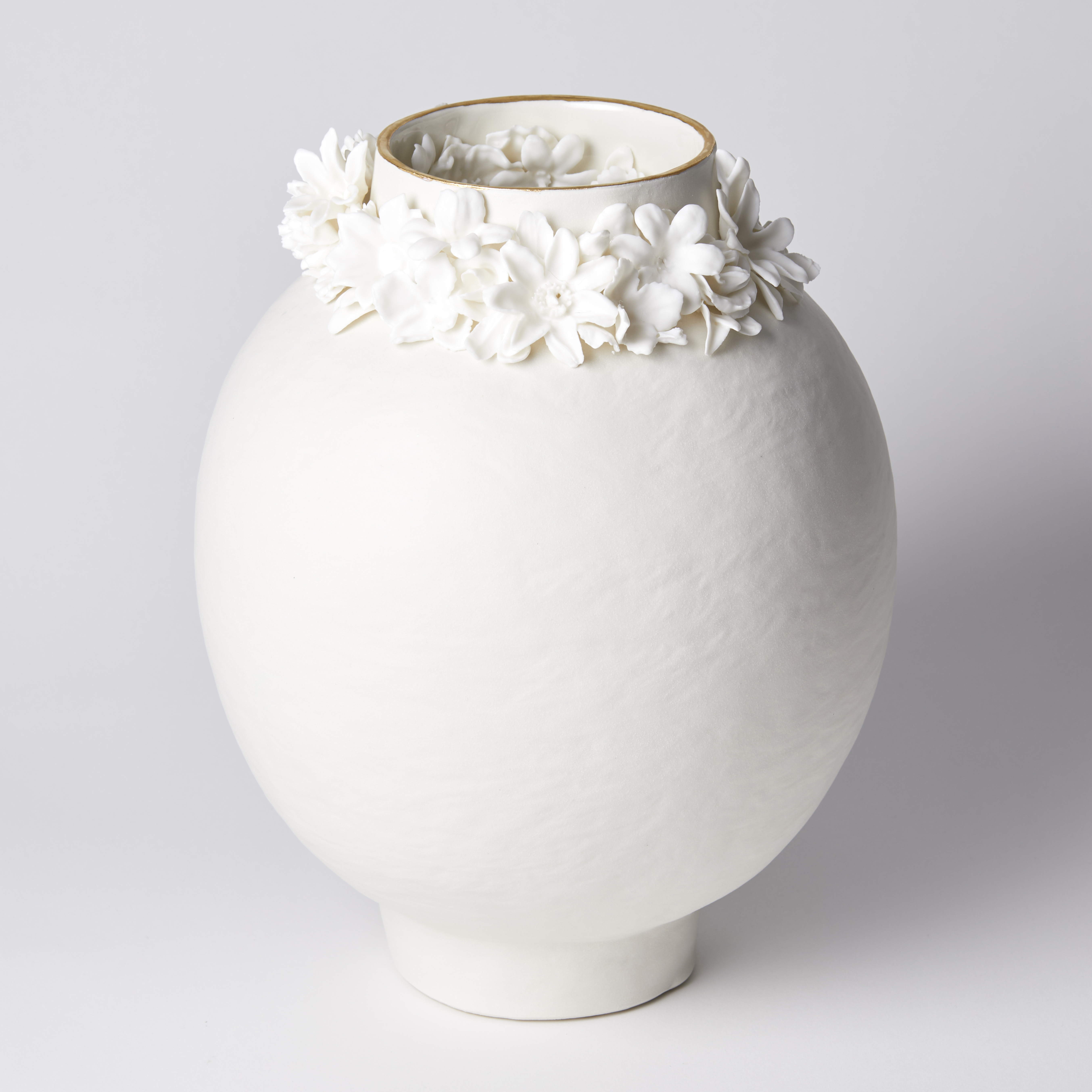off white rounded vase with slightly rough texture and foot ring with flowers clustered round the neck opening with a final rim of gold lustre handmade from porcelain and parian