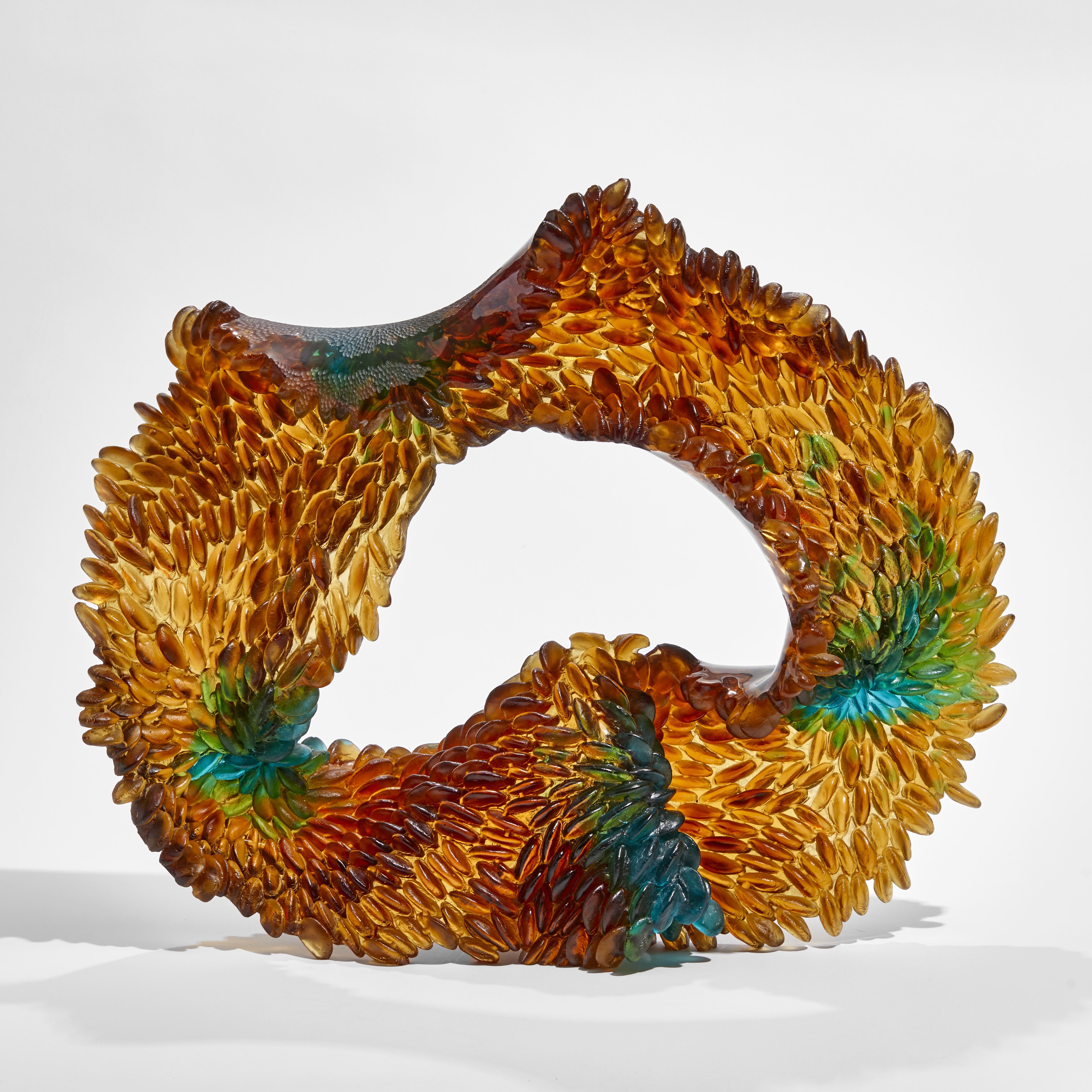 amber and green oval standing sculpture with one side with raised leaflike texture the other side smooth hand made from glass