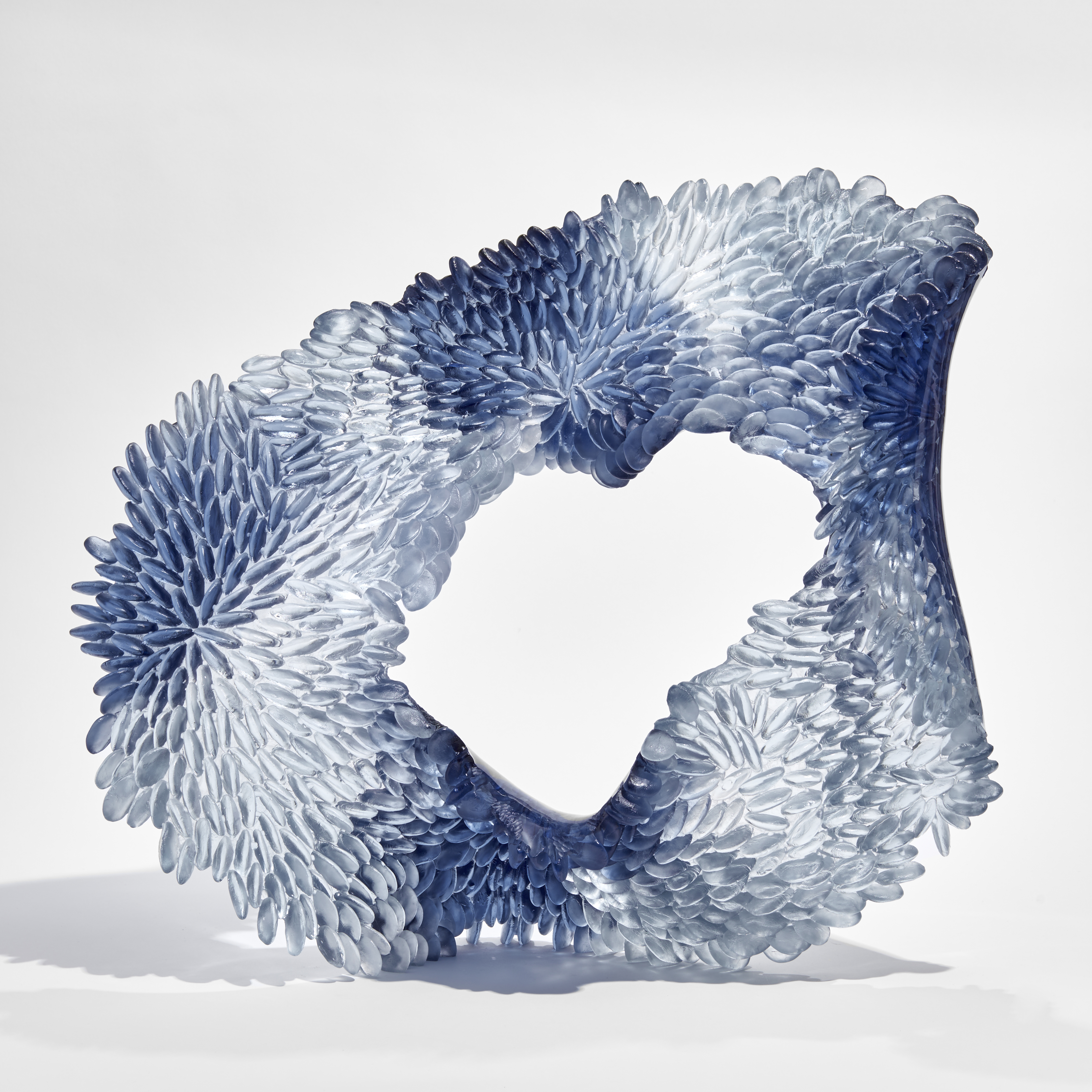 indigo blue and clear uneven standing ring sculpture with one side with raised scaly surface the other side smooth hand made from glass