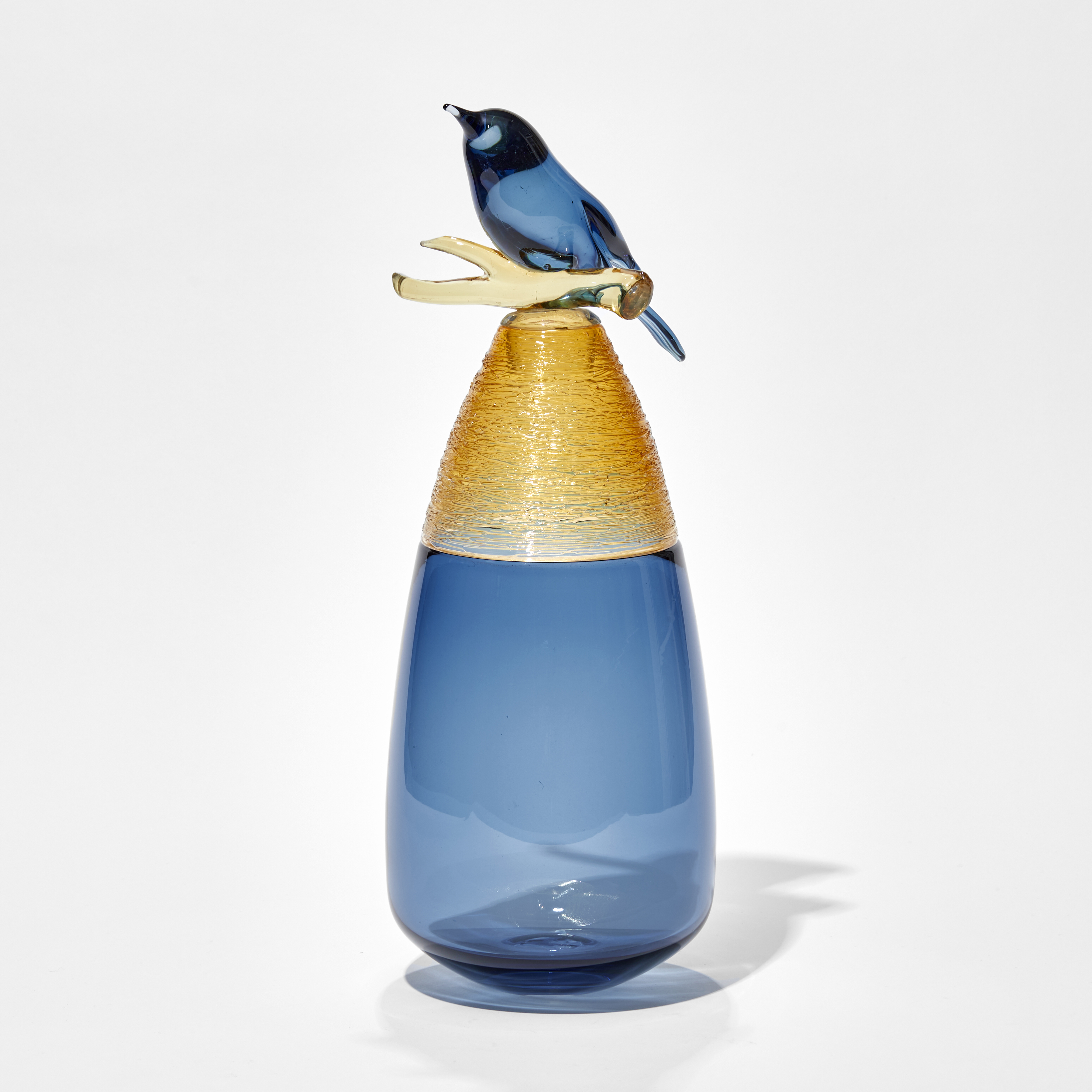 blue teardrop shaped vase with the top third section in amber with woven spun texture and a stopper with a perched blue bird with yellow branch hand made from glass