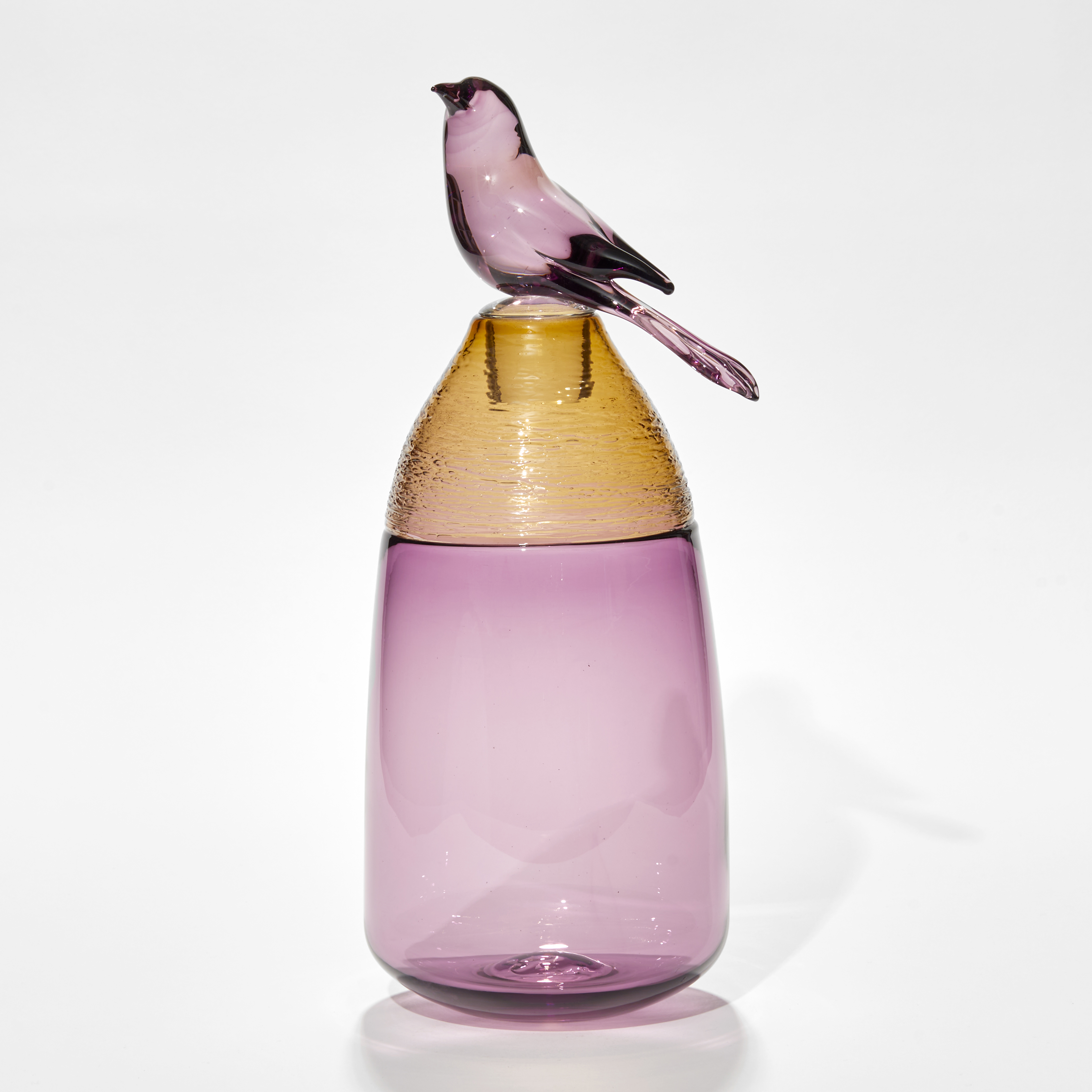 transparent purple vessel with amber top section with fine raised cane detail and purple bird shaped stopper on the top hand made from glass