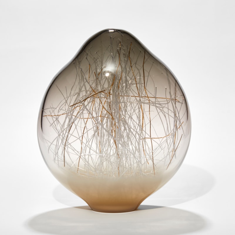 Amorphic shaped sculpture in transparent warm grey fading to clear then opaque taupe with organic canes in white and gold trapped inside hand made from glass