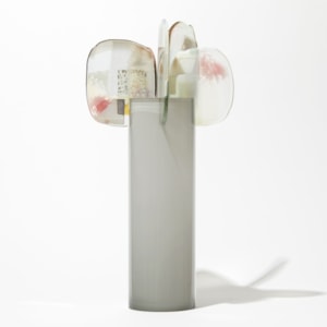 soft grey glossy cylinder with five perched abstract petals at the top each with patches of colour in pink grey opal white and gold hand made from glass