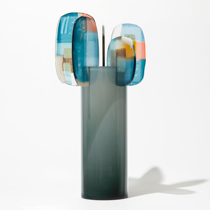 shiny fading from dark to light grey at the top cylinder with rounded leaves at the top with abstract patterns in teal blue pink opal white and gold hand made from glass