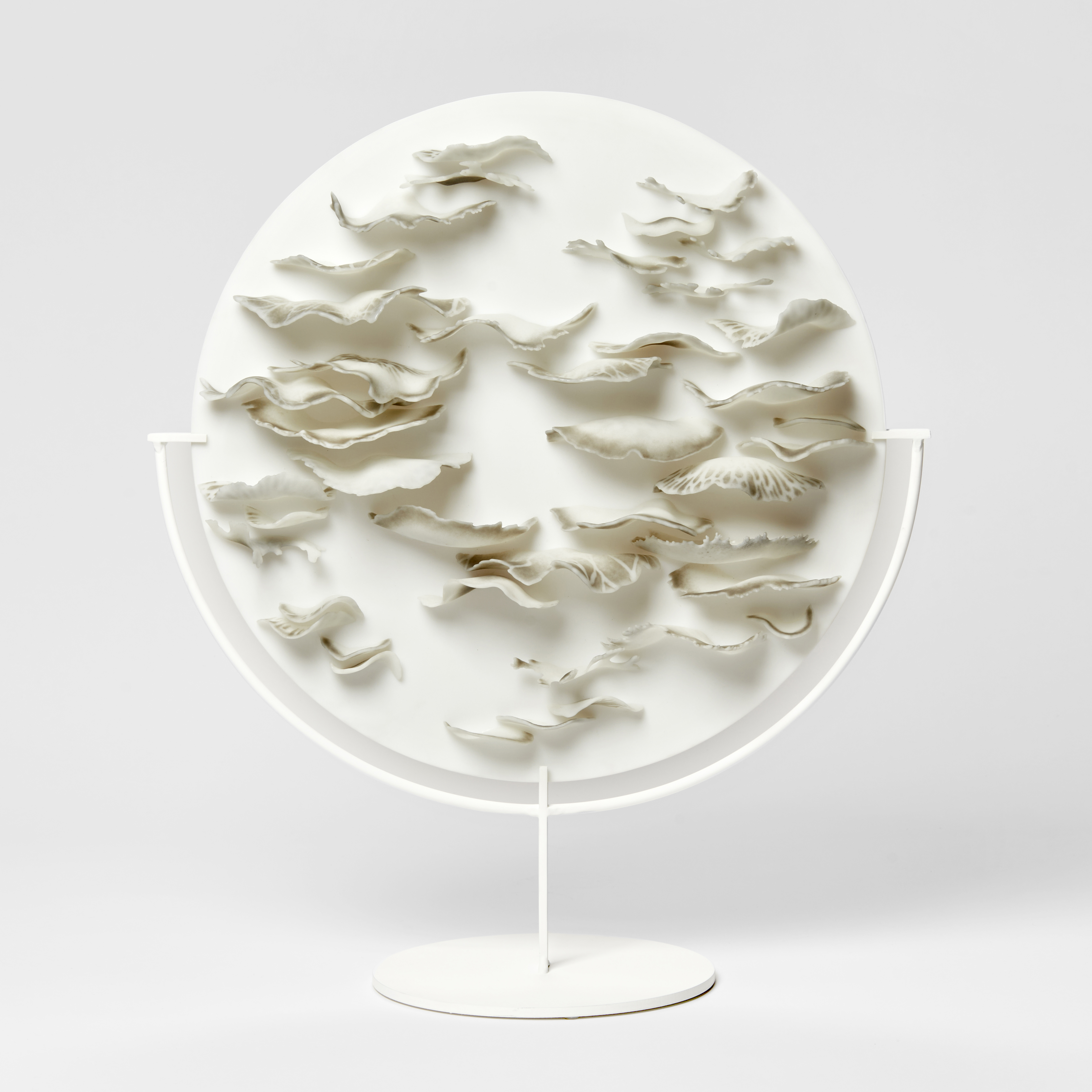 round opaque white plate with protruding half mushroom caps with wavering fronds in earthy tones of brown grey and taupe hand made from glass on a white stand