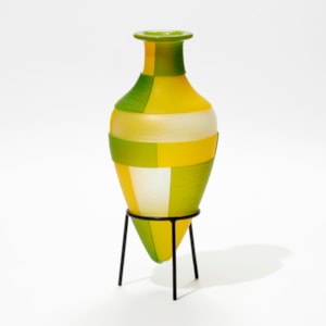 green and yellow amphora bottle with geometric square cut bold patterns on a black steel tripod stand handmade from glass
