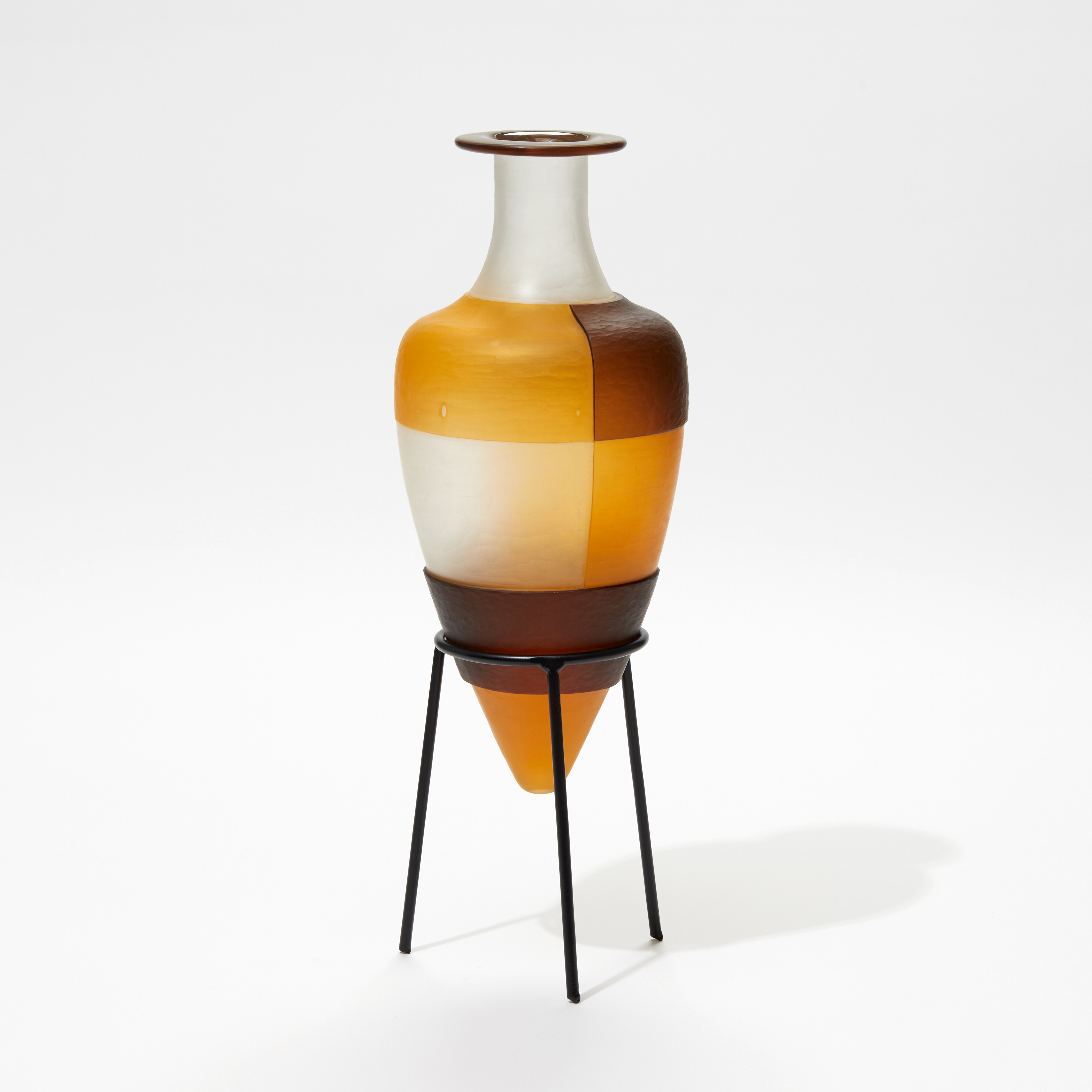 clean orange and brown bottle with block geometric square cut pattern perched on a black metal stand handmade from glass