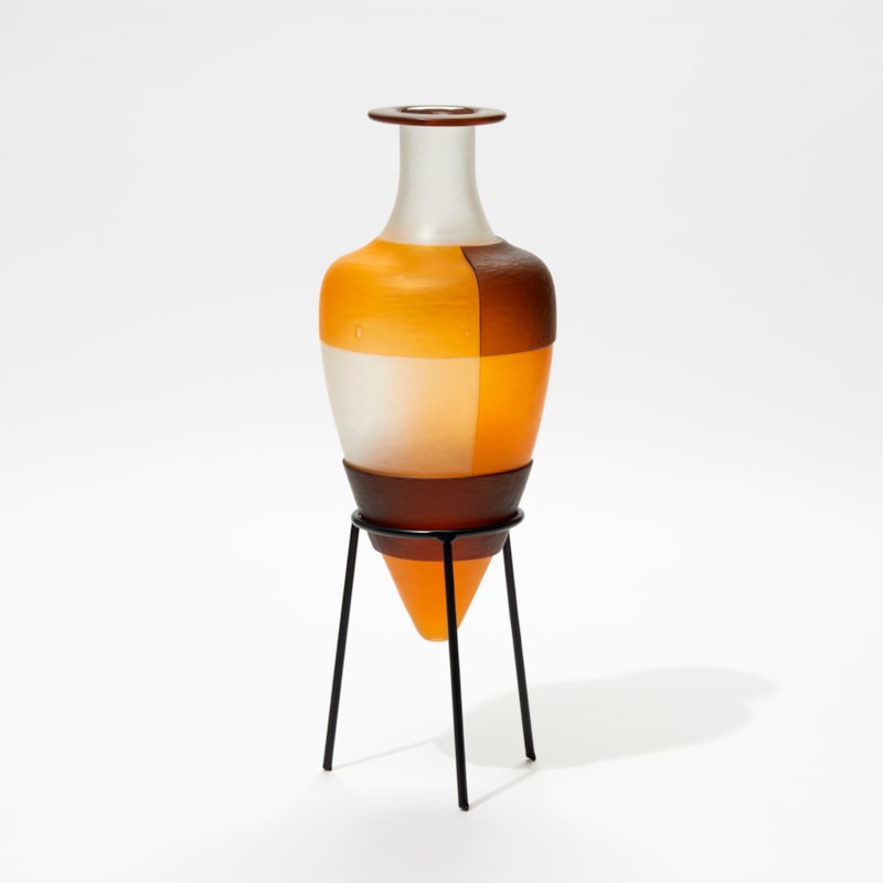 clean orange and brown bottle with block geometric square cut pattern perched on a black metal stand handmade from glass