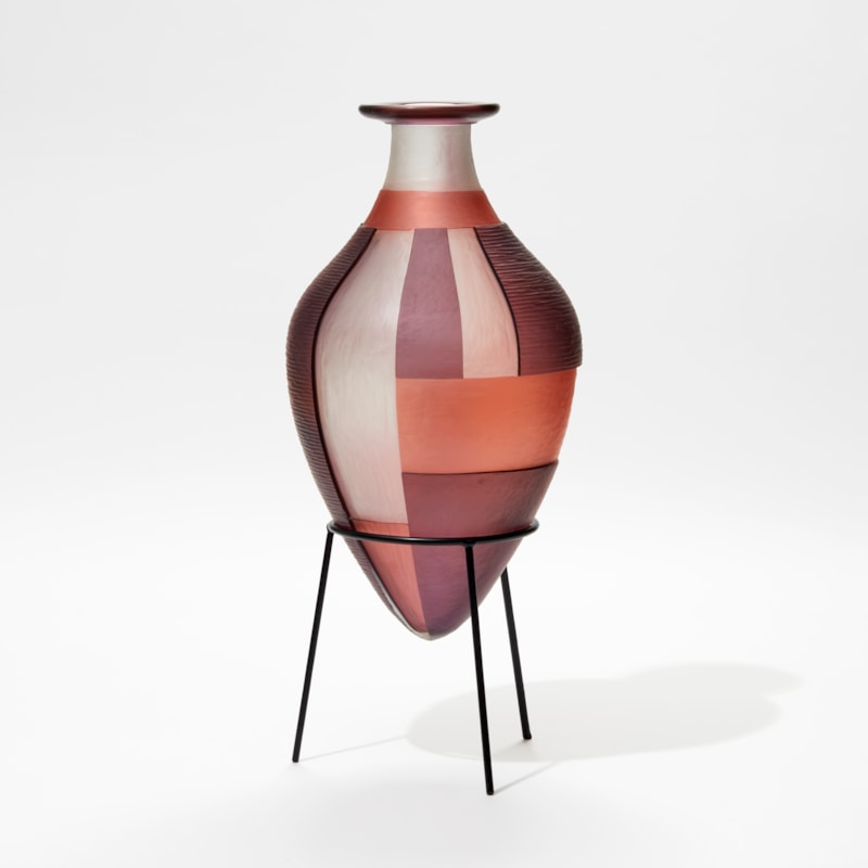 aubergine clear and pink bottle with wide top lip and pointed bottom with block bold pattern sat within in a black steel stand hand made from glass