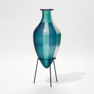 blue jade and white elongated bottled with pointed base and wide rim and an abstract block cut pattern hand made from glass with a black steel stand