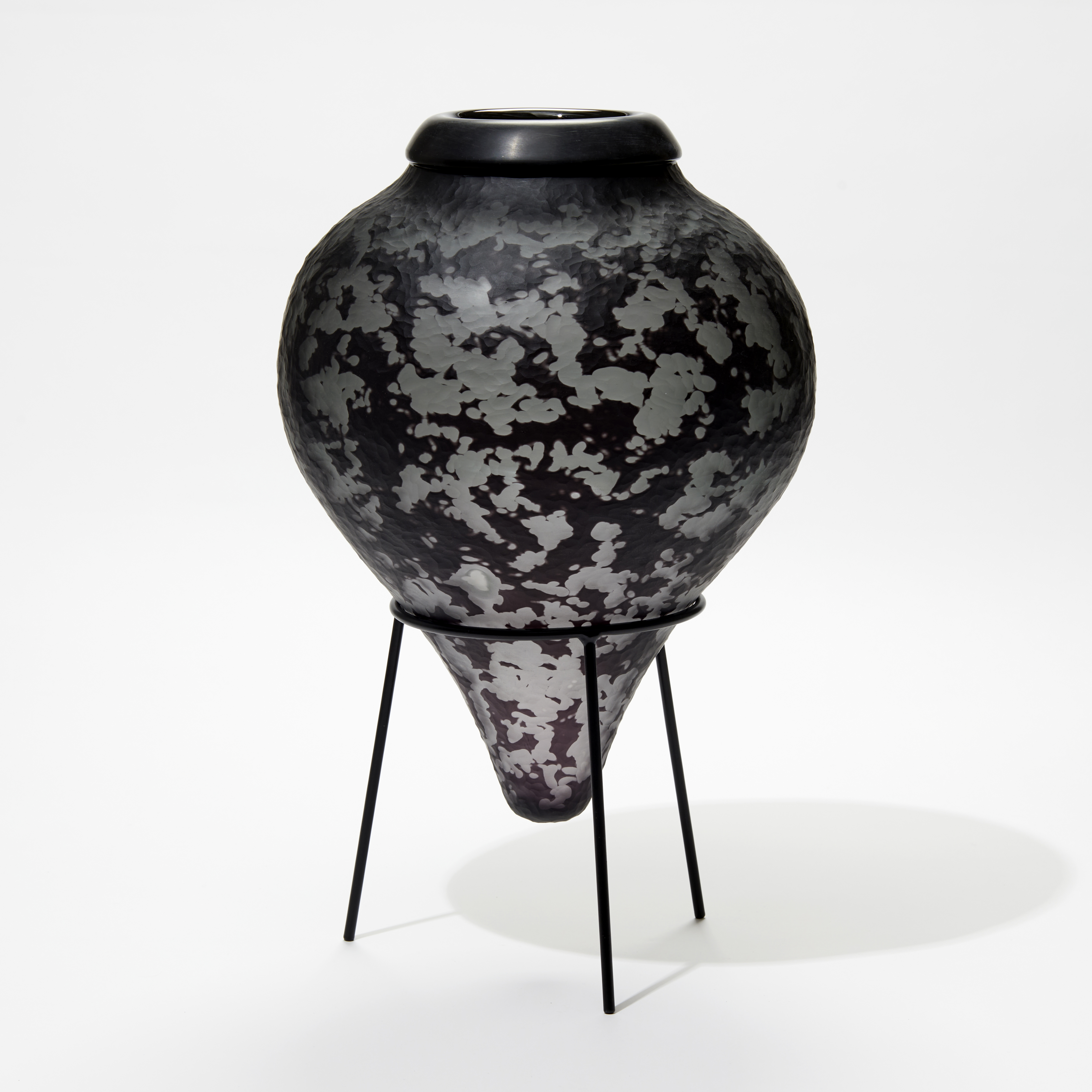 dark grey and black inverted teardrop bottle with textured surface and black cuff opening on a black tripod stand