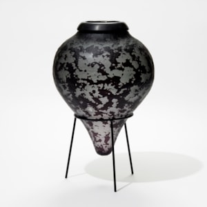 dark grey and black inverted teardrop bottle with textured surface and black cuff opening on a black tripod stand