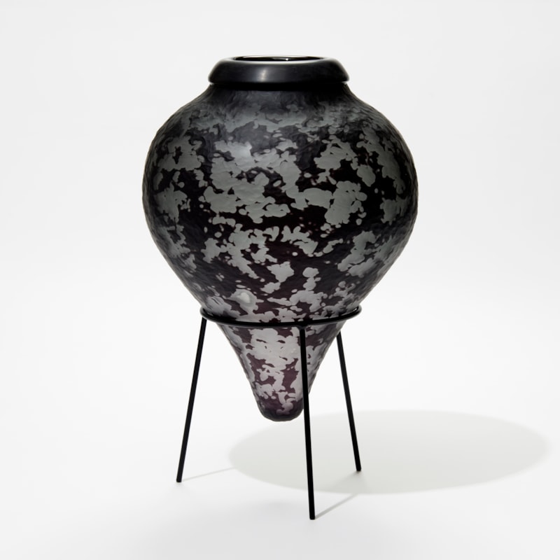 dark grey and black inverted teardrop bottle with textured surface and black cuff opening on a black tripod stand