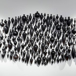 hundreds of black handblown and polished small amphora bottles wall mounted and hung in a clustered pointed horizontal oval configuration