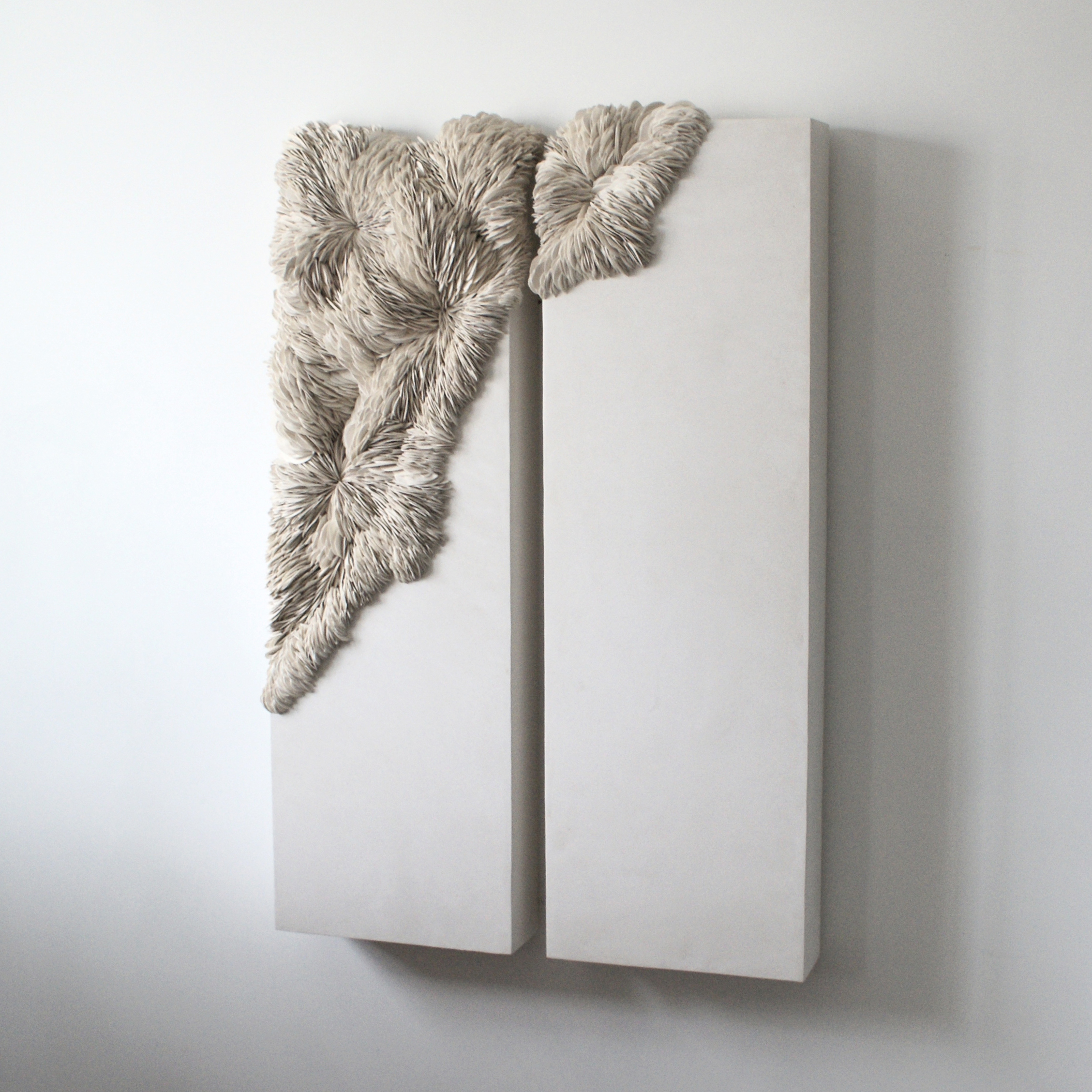 twinned large long rectangular wall mounted light grey stone like sections with organic raised shard detail in the two left corners moving from one panel to the next hand made from porcelain and tadelakt plaster 