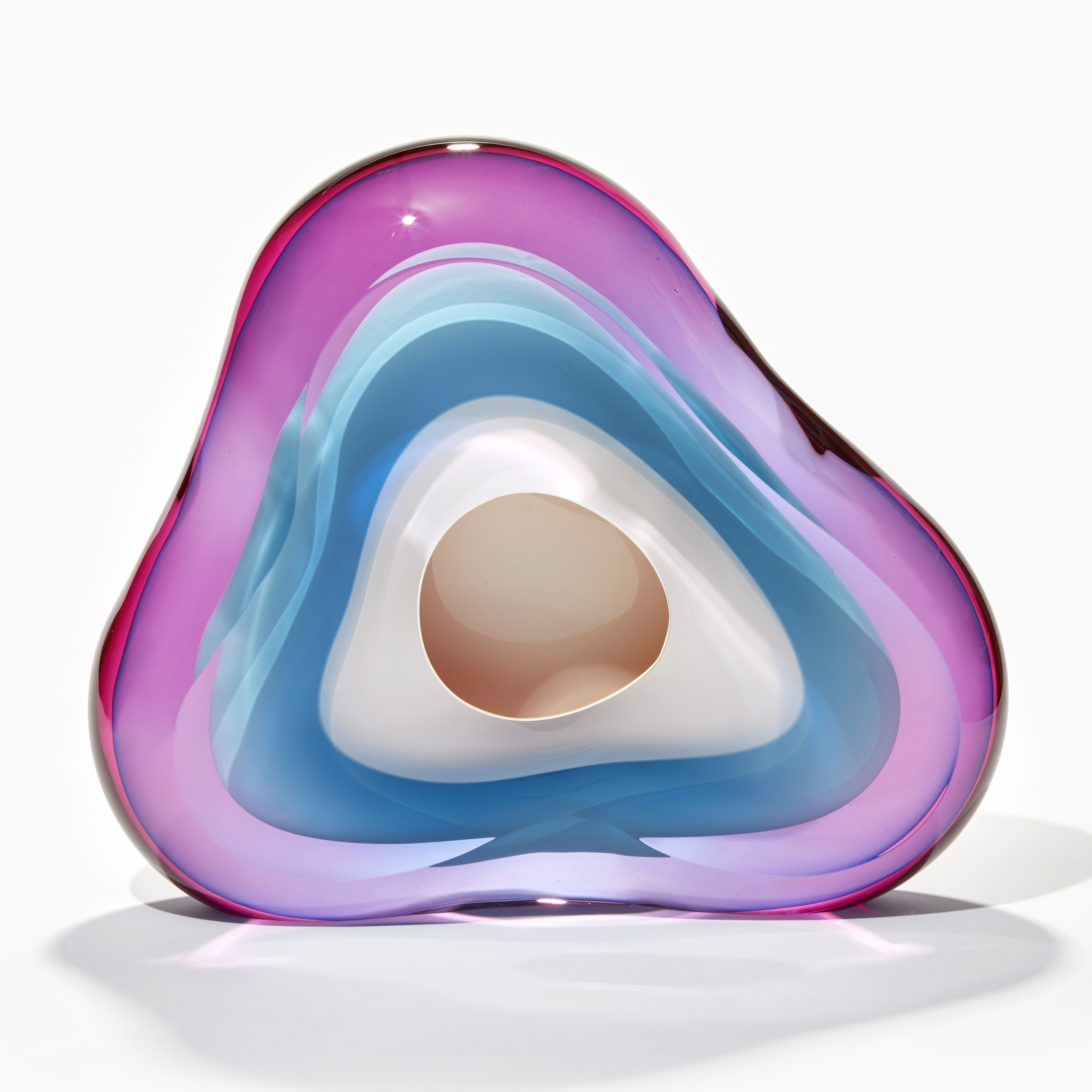 soft fluid triangular standing shape with interior cavity lined in brilliant white that is surrounded in transparent layers in turquoise and pink which merge creating further hues handmade from glass