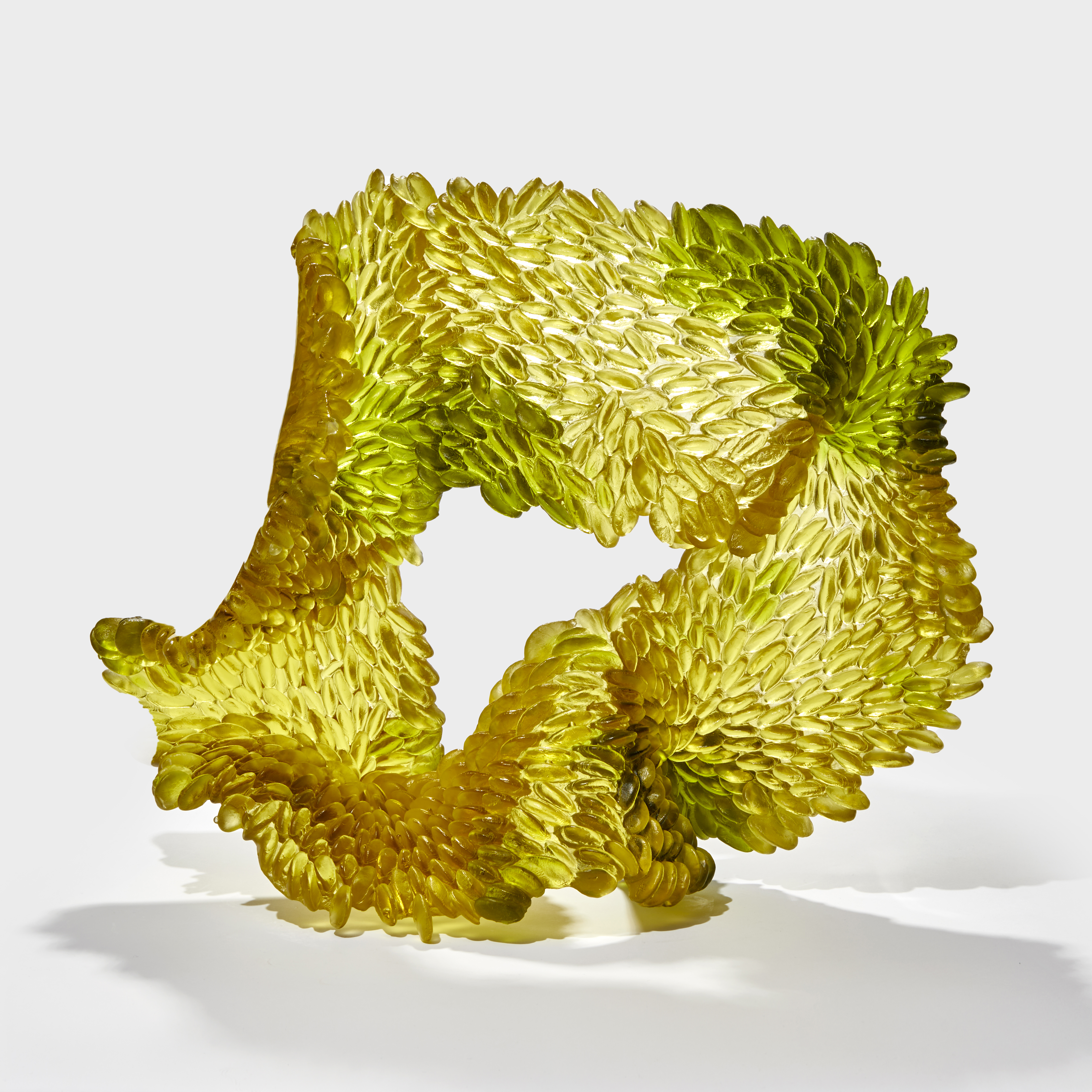 standing organic textured abstract form with central opening in olive green and gold yellow with one side shiny the other textured with raised rounded oval scales hand made from glass