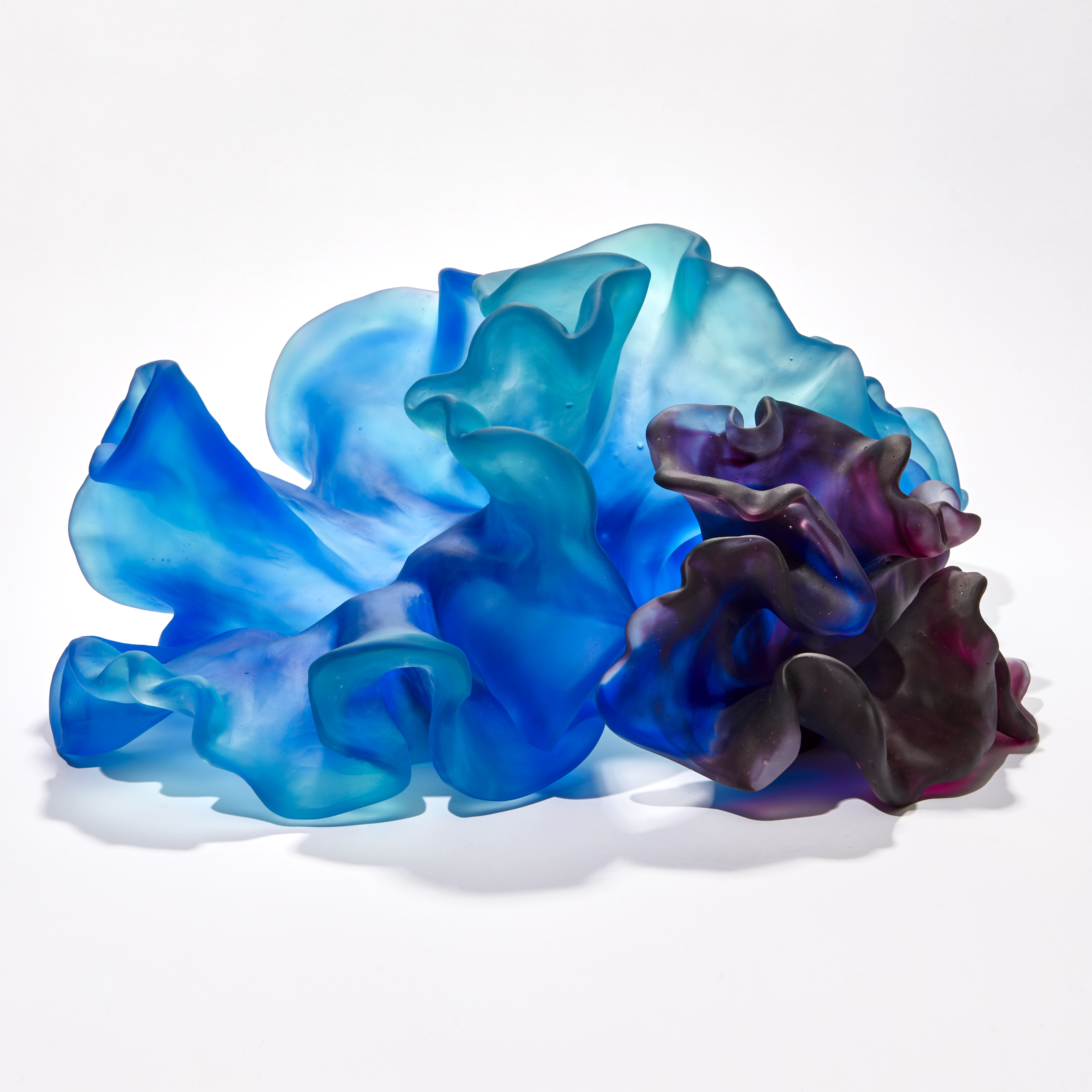two coral interlocking forms one intense blue the other rich deep purple with the appearance of coral with smooth surfaces and frilled edges hand made from glass