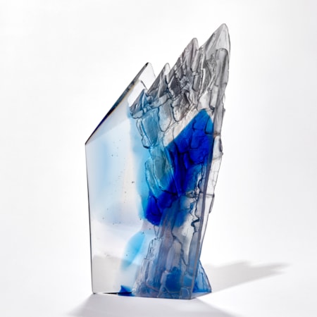 transparent angular sculpture with rugged cliff face detail with areas in light and dark blue hand made from cast glass
