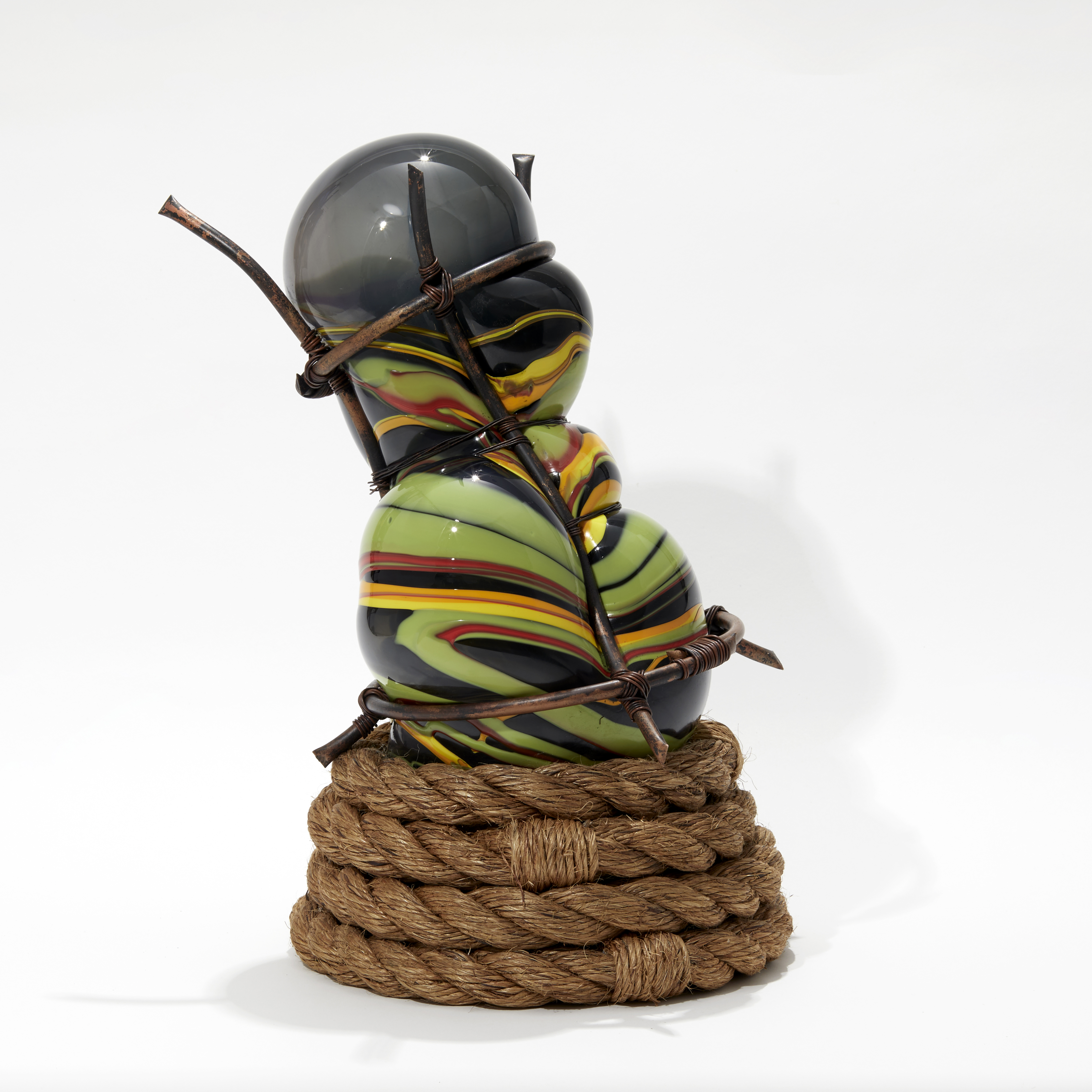 hand blown glass bulbous sculpture in grey and mixed banded african colours of red yellow and green with wound rope base and set within a copper cage