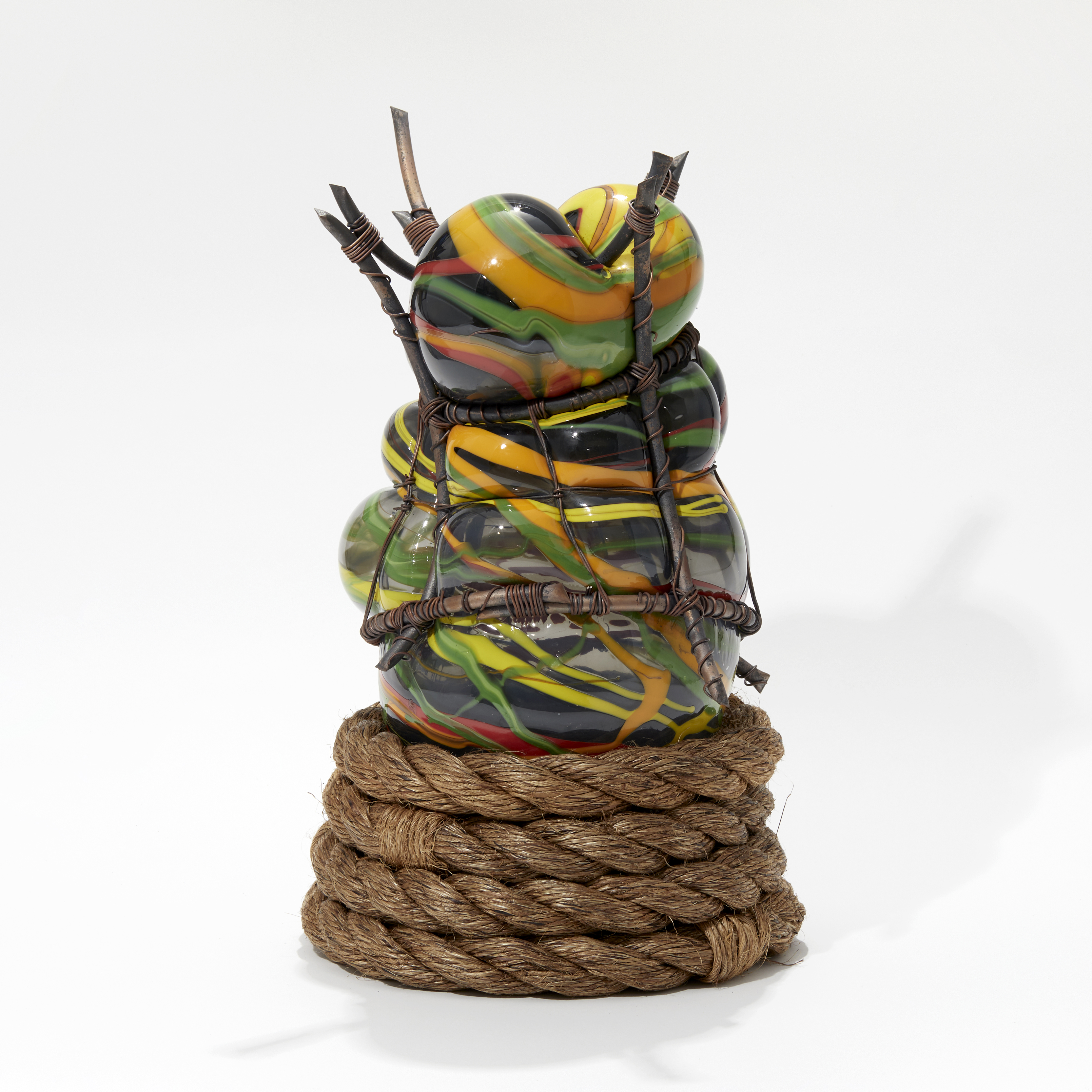 orange green yellow and black bulbous hand made glass sculpture held within a copper cage with a wounded rope at the base