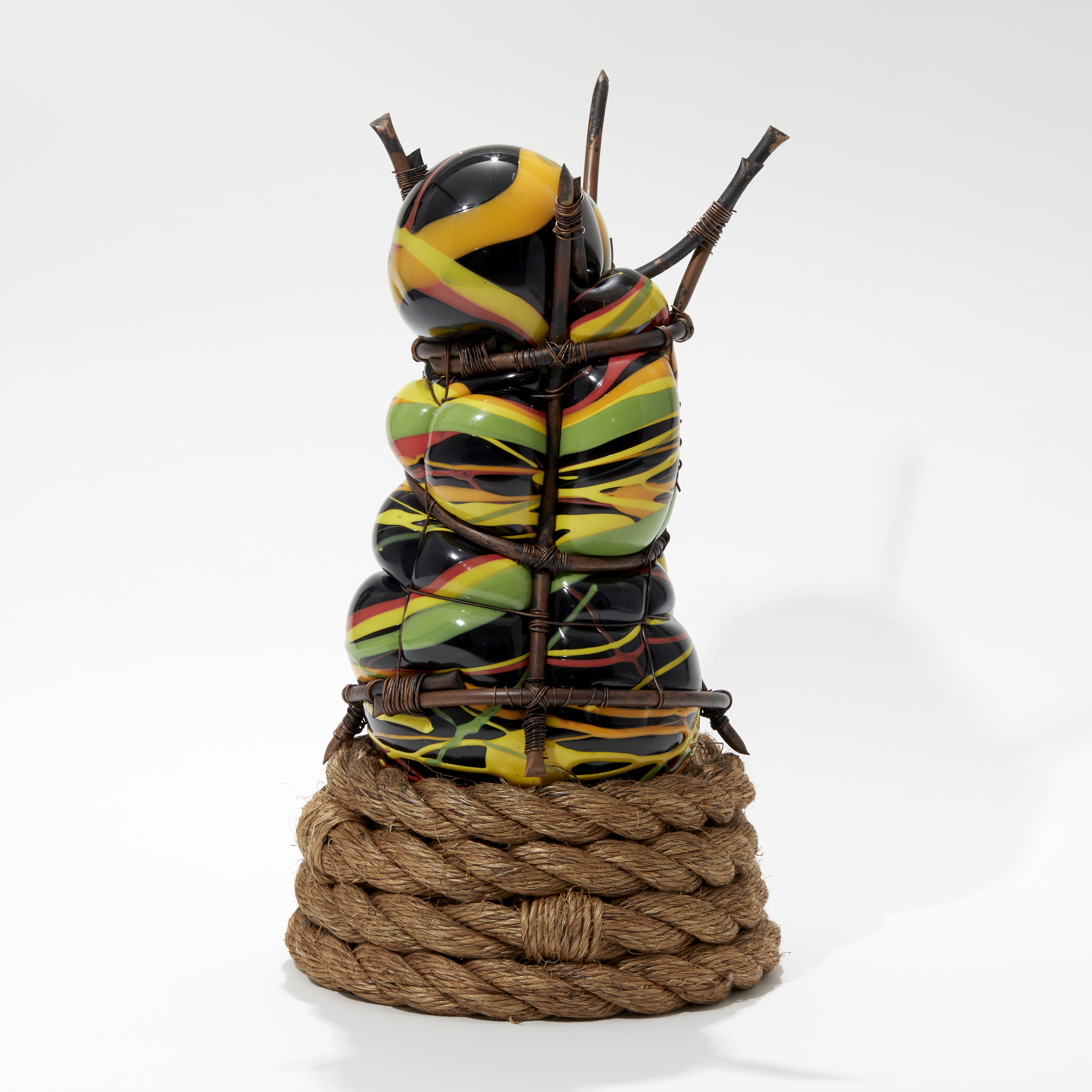 hand made glass sculpture blown in to a copper cage with the appearance of bursting through in black orange green and yellow with coiled rope base